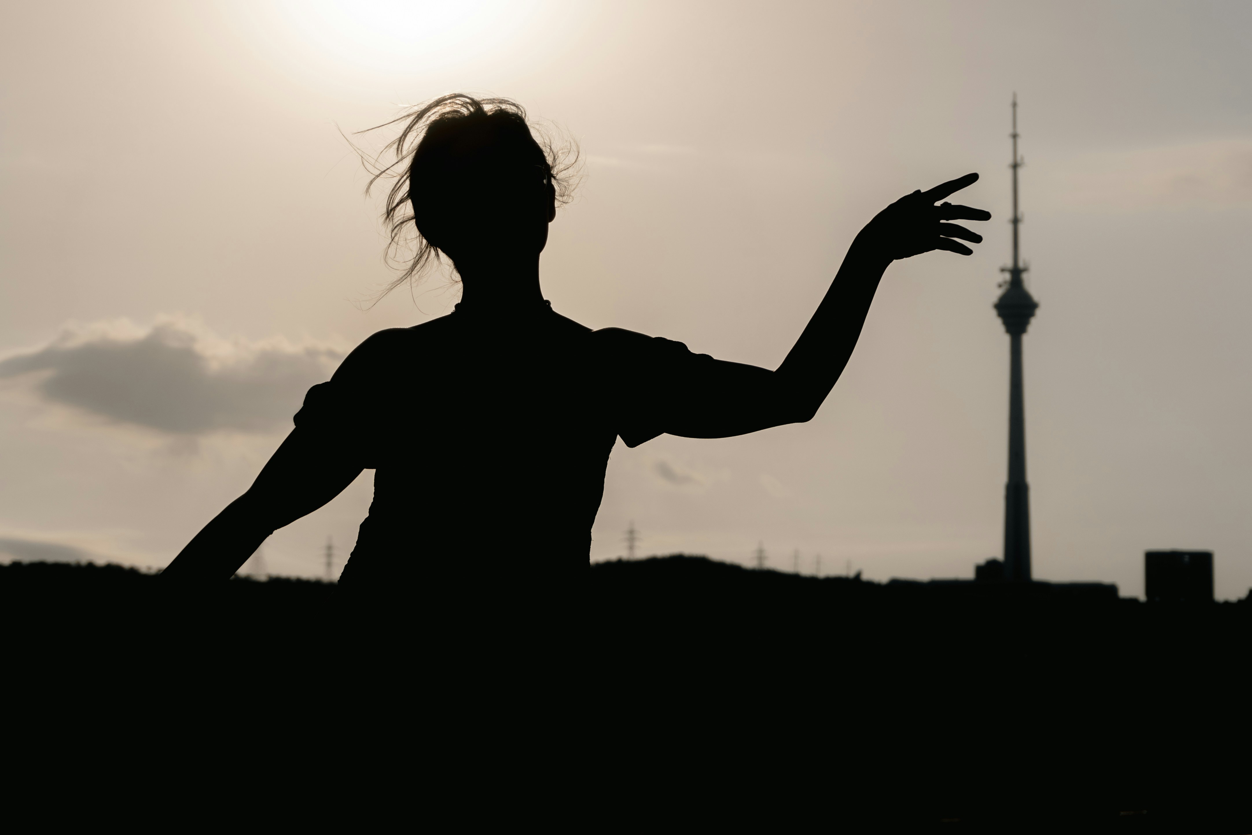 A person in silhouette against a bright sky with a tall television tower