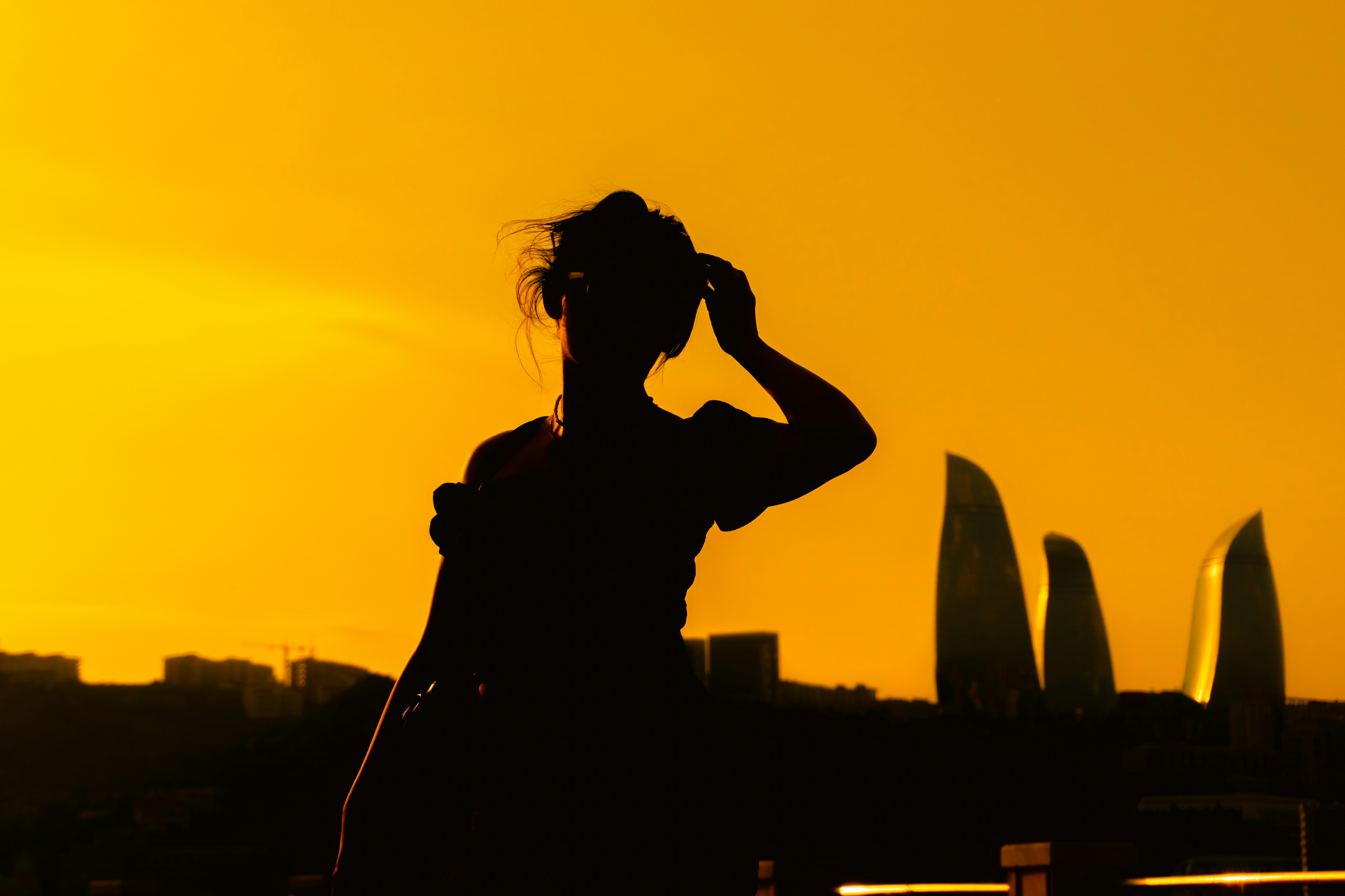 A person in silhouette against a warm orange sky with the Flame Towers in Baku