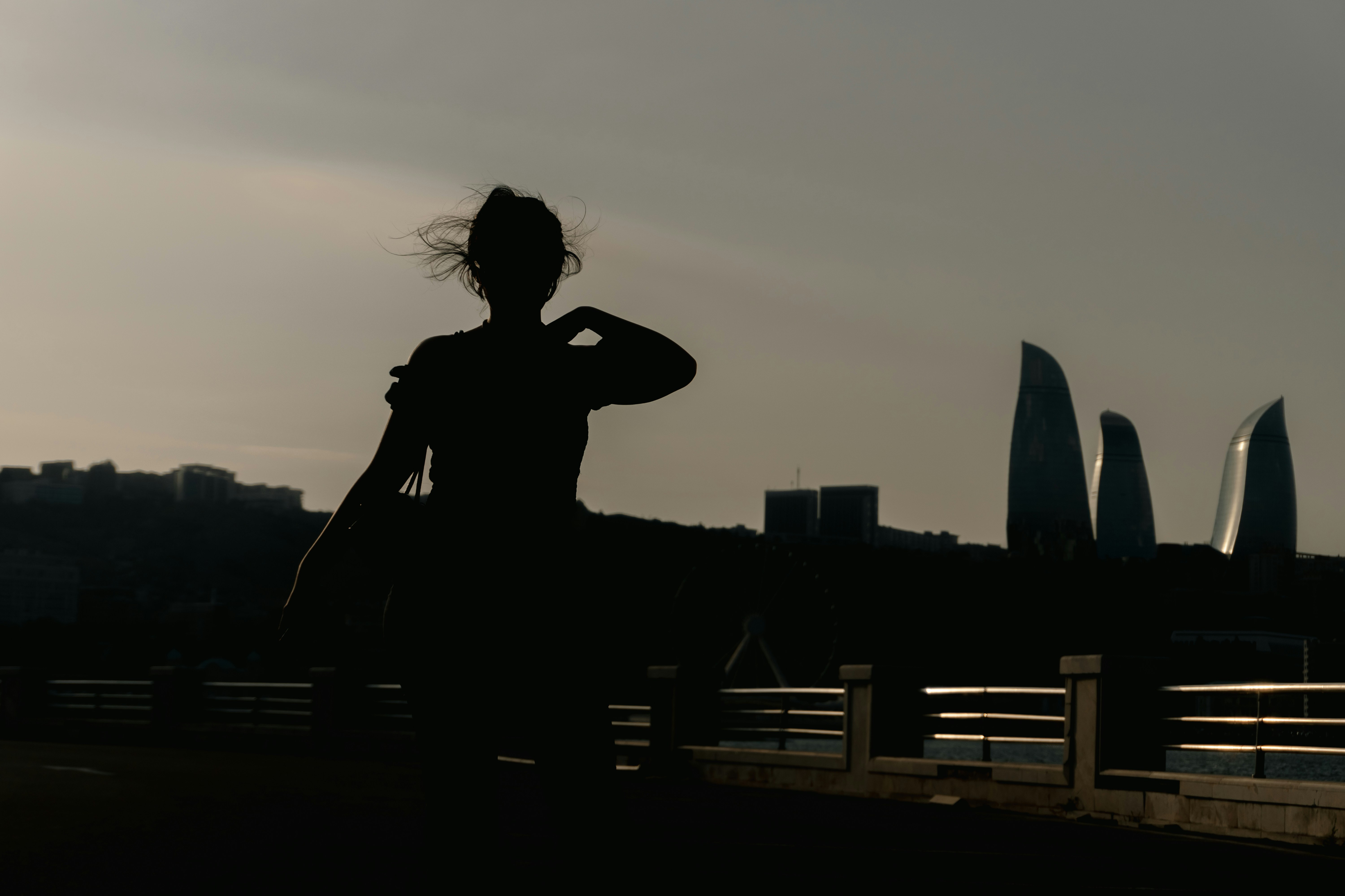 A person in silhouette against a grey sky with the Flame Towers in Baku