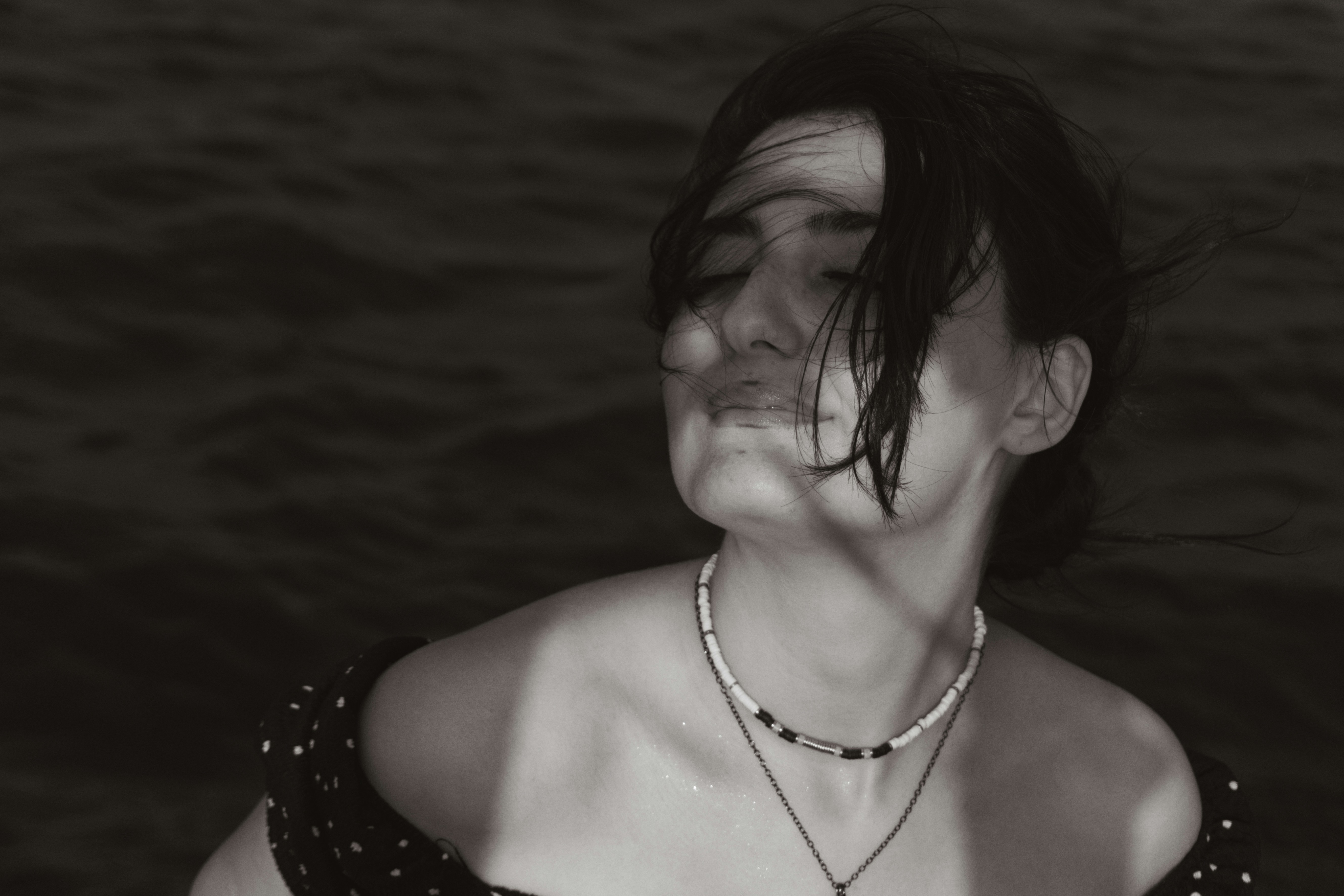 A woman with windblown hair and eyes closed against dark water