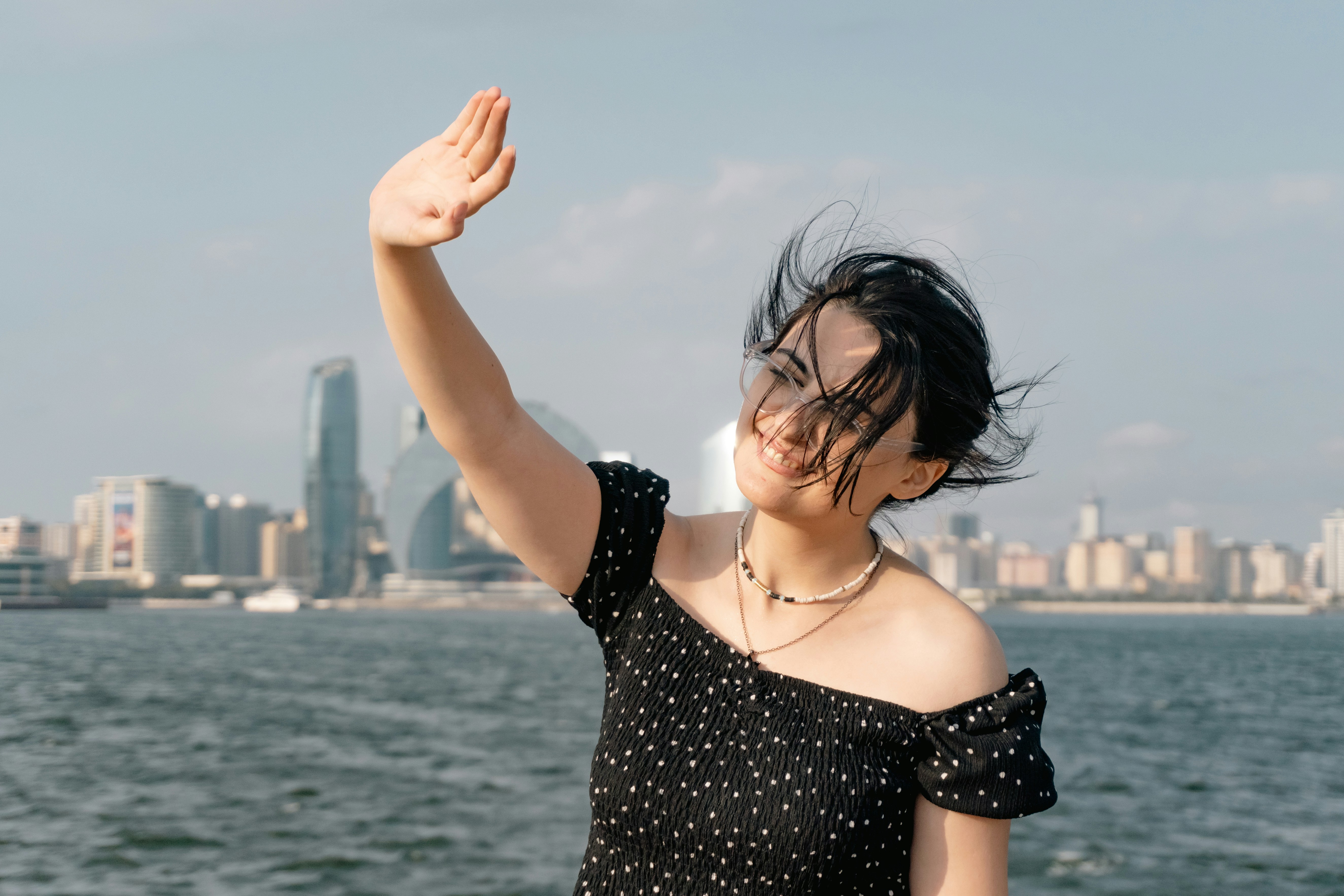 A woman in a black polka dot top waving against a city skyline