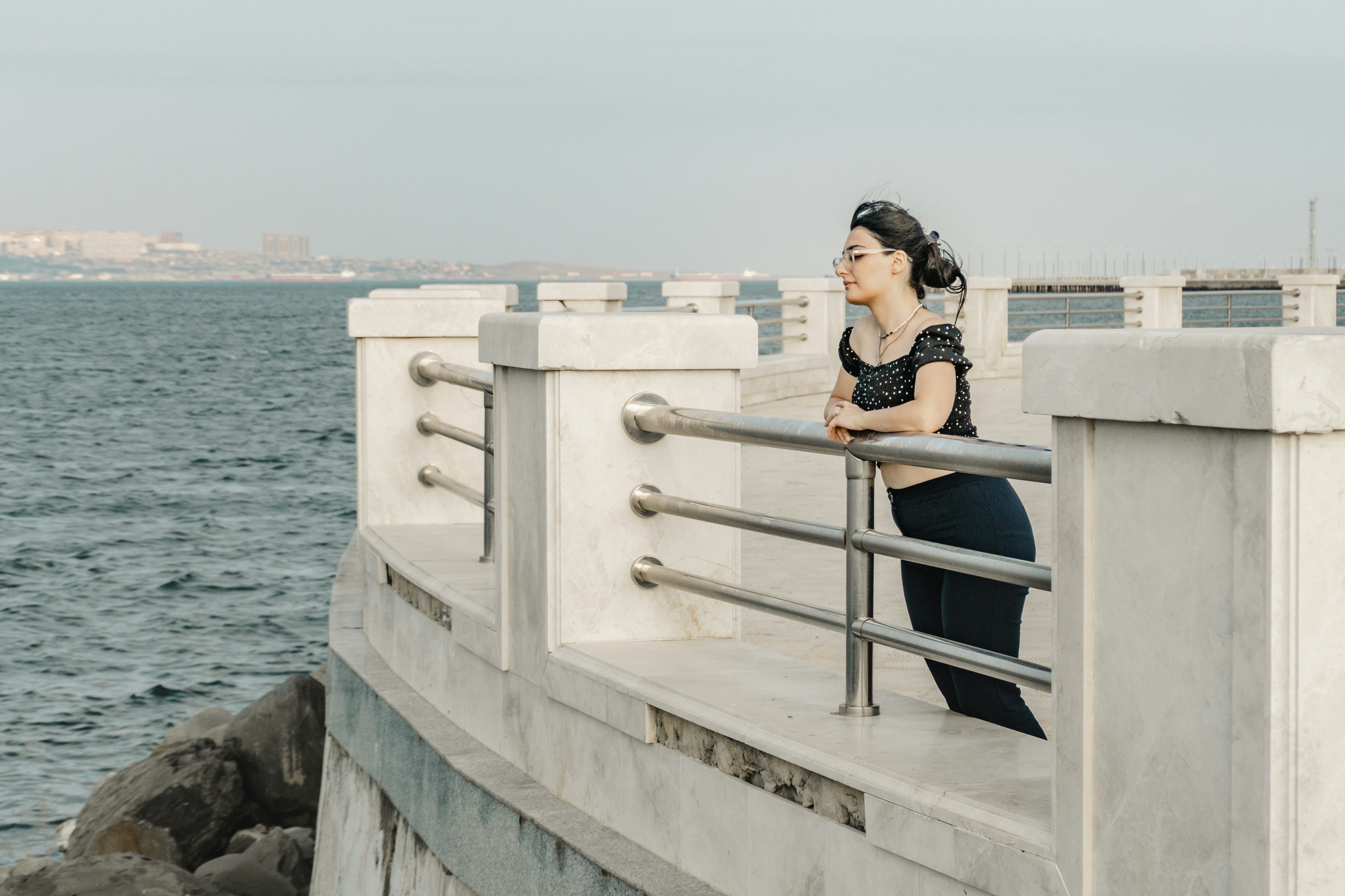 A woman in a polka dot top leaning on a stone railing by the sea