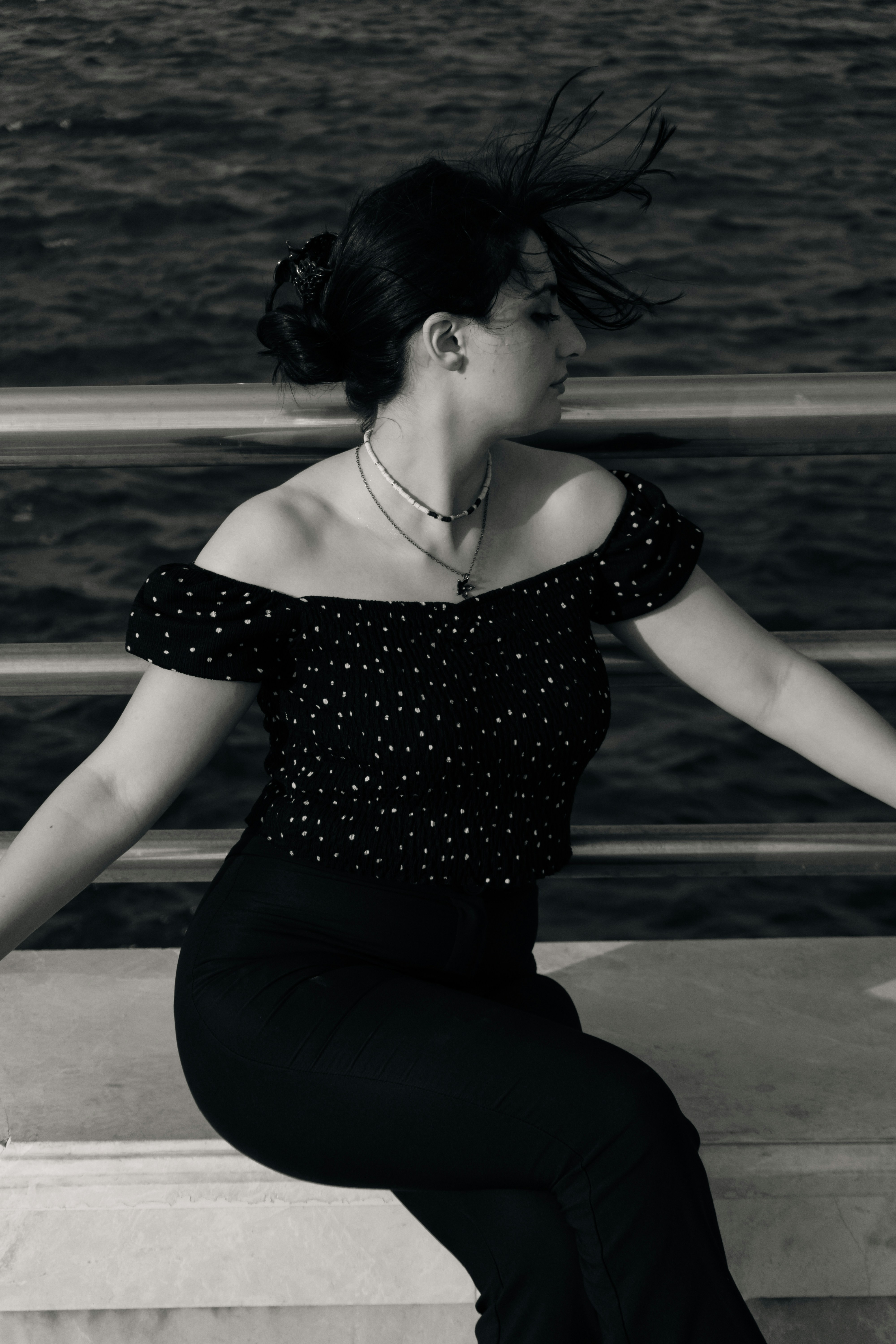 A woman in a black polka dot top sitting by a dark water railing