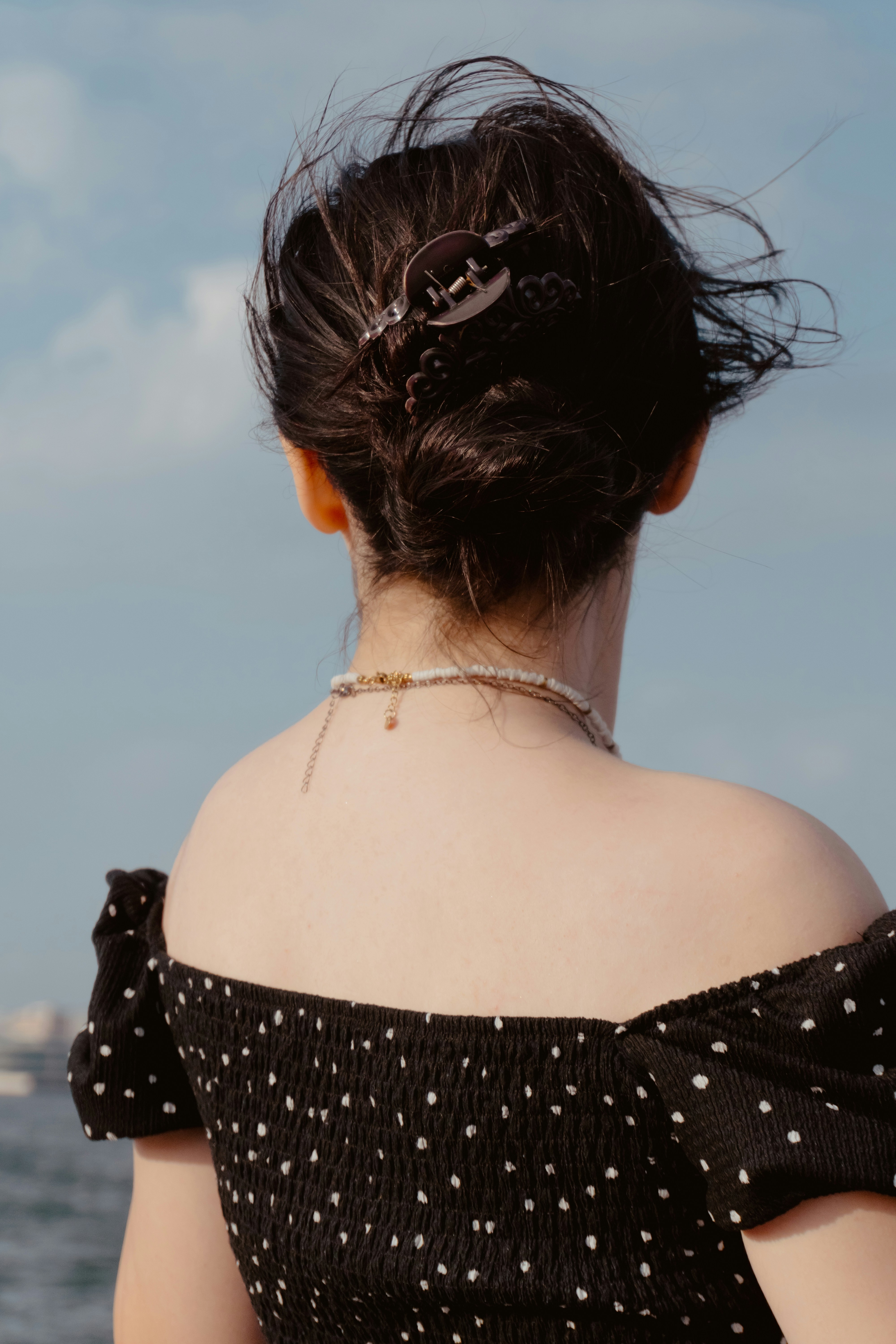 A woman with hair in a clip against a blue sky and water
