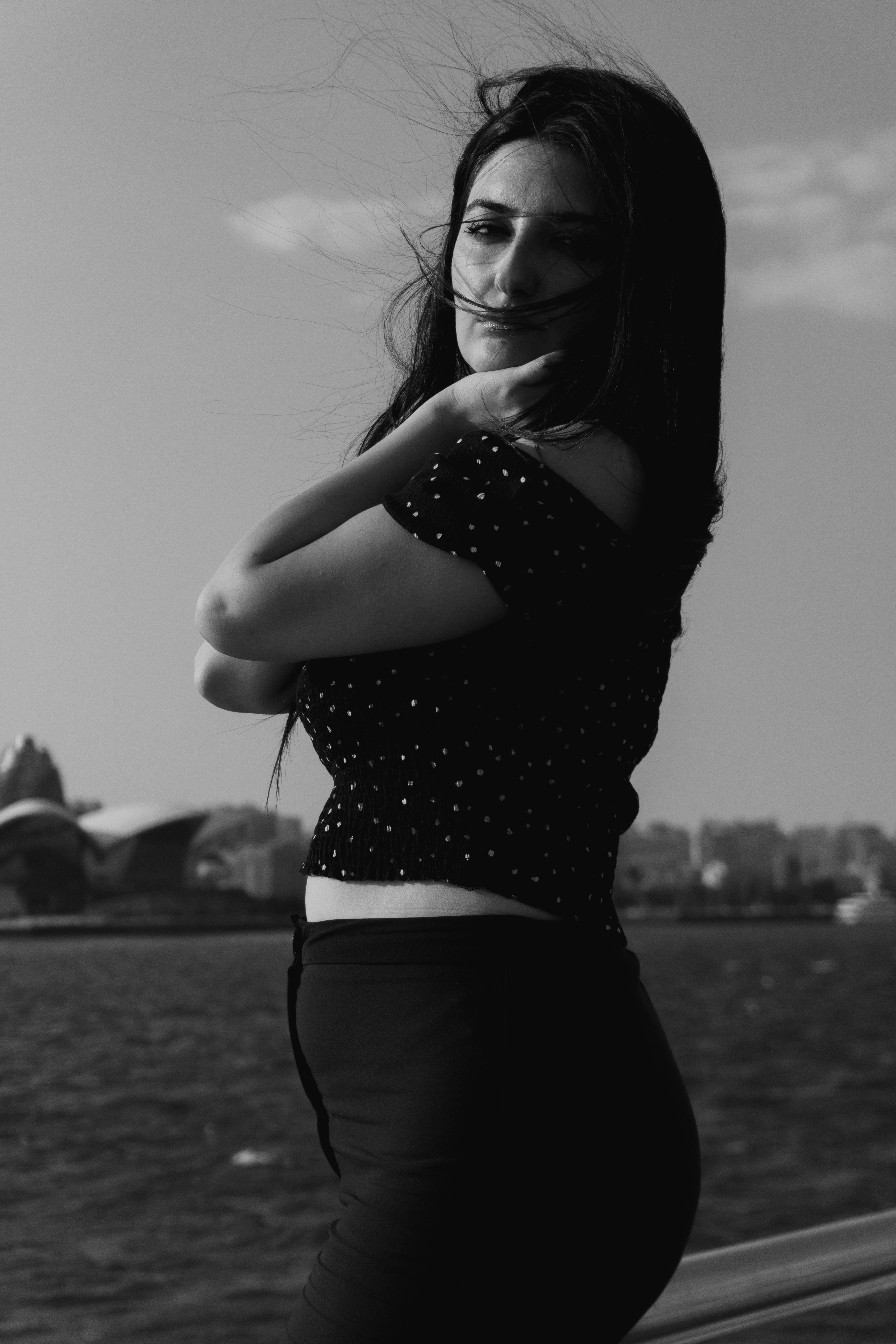 A woman in a polka dot top standing by a river with city buildings