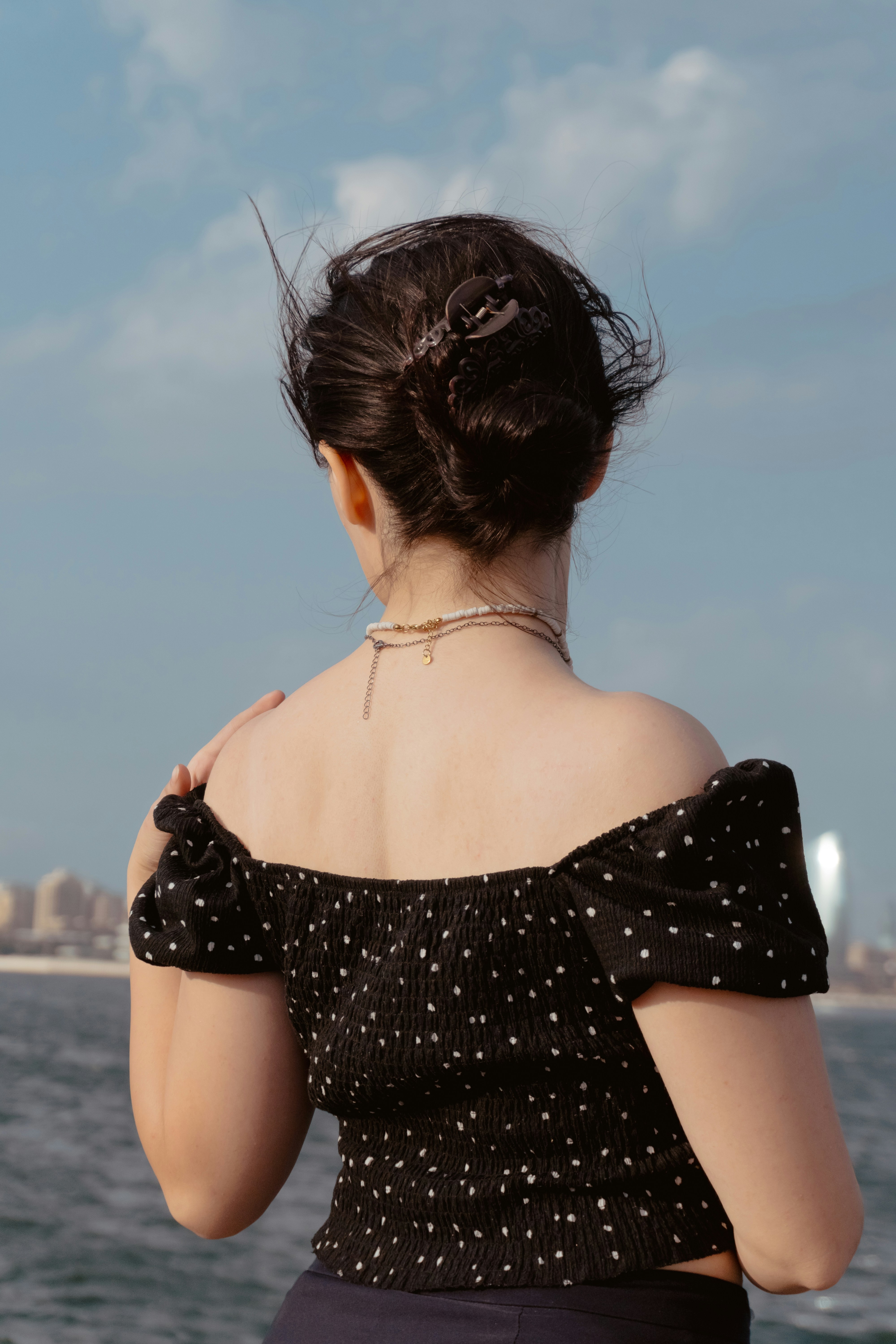 A person in a black polka dot top against a blue sky and water