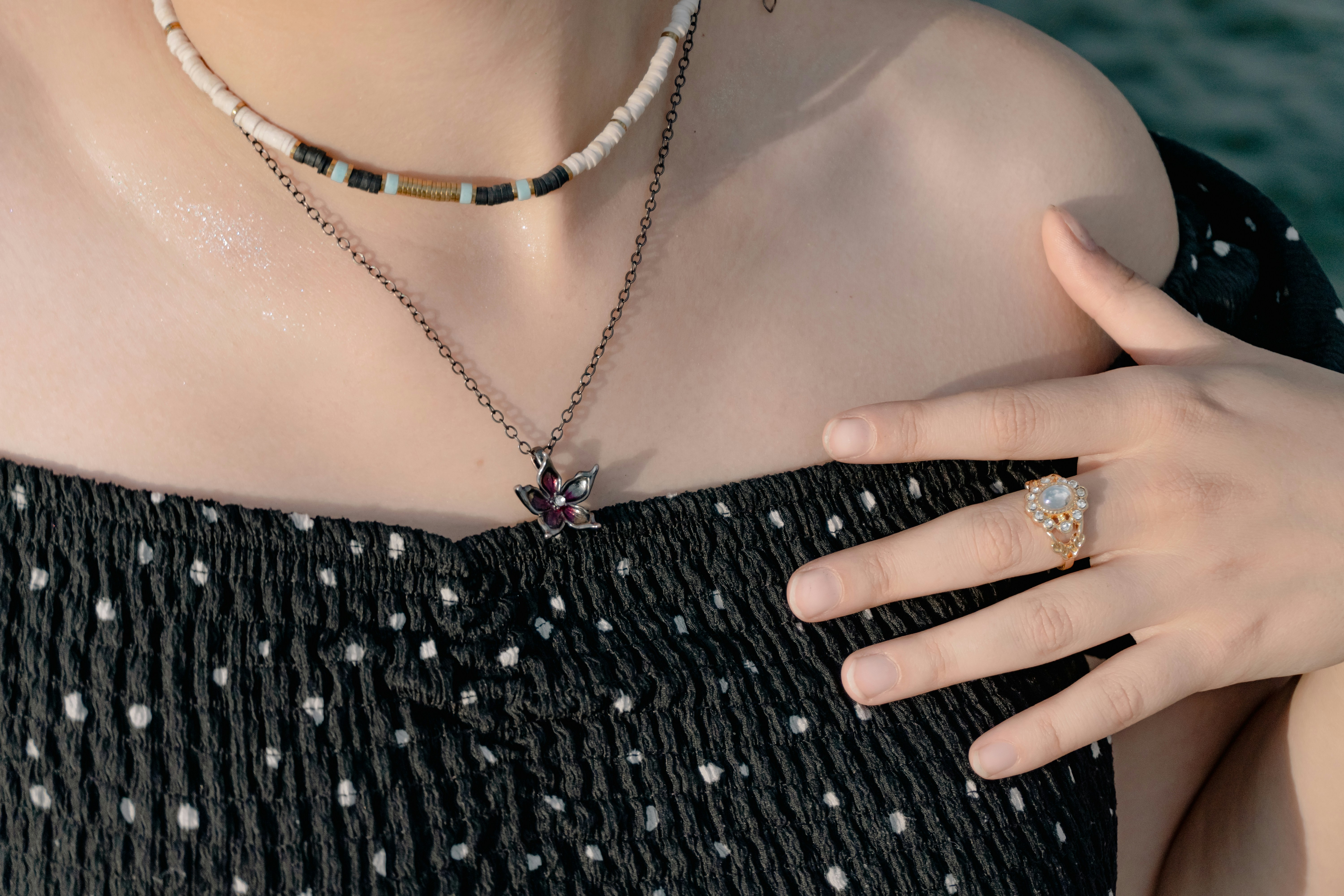 A person wearing a beaded necklace, a flower pendant, and a gold ring
