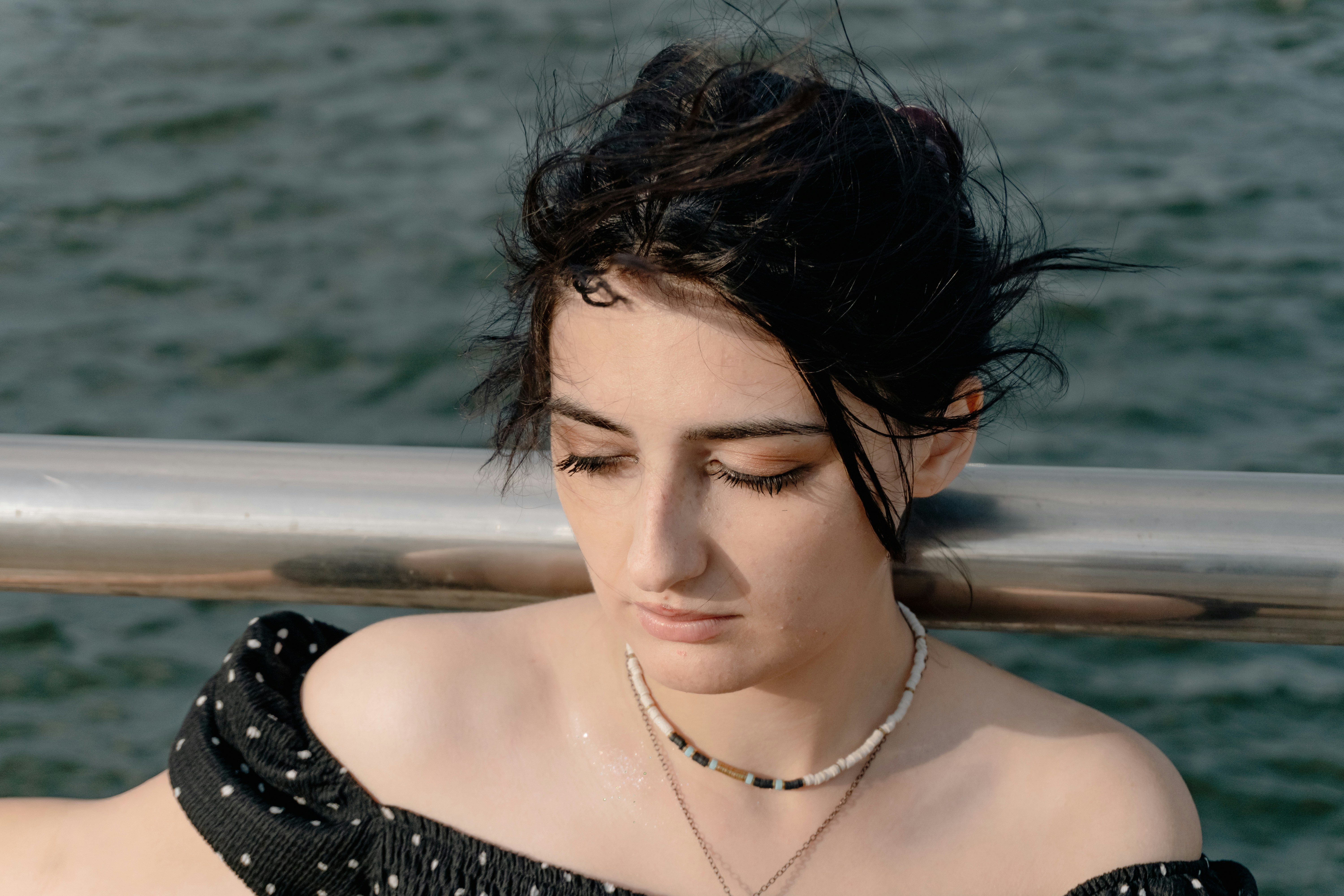 A woman with dark hair in a black polka dot top by the water