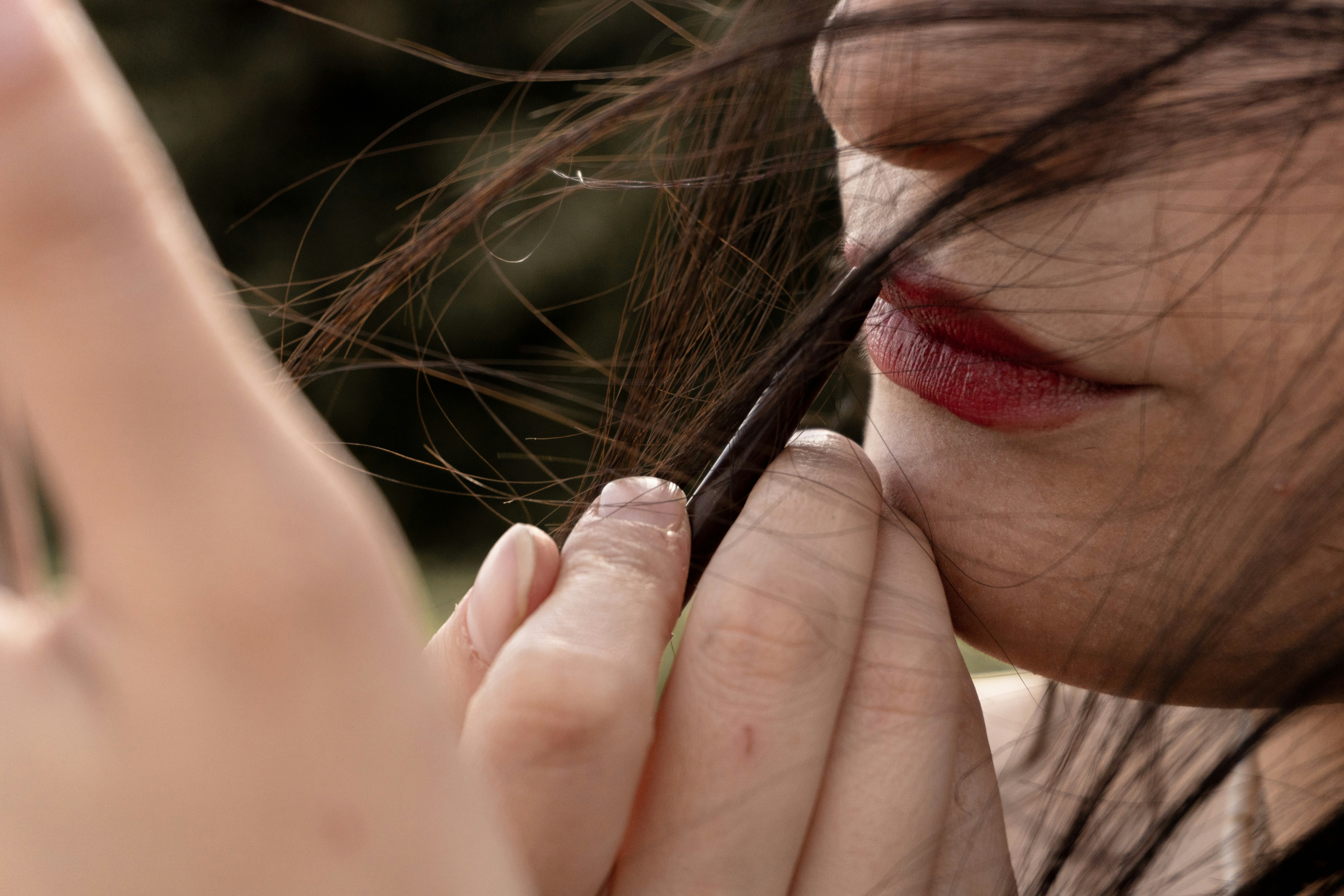 A person holding a strand of dark hair near their red lips