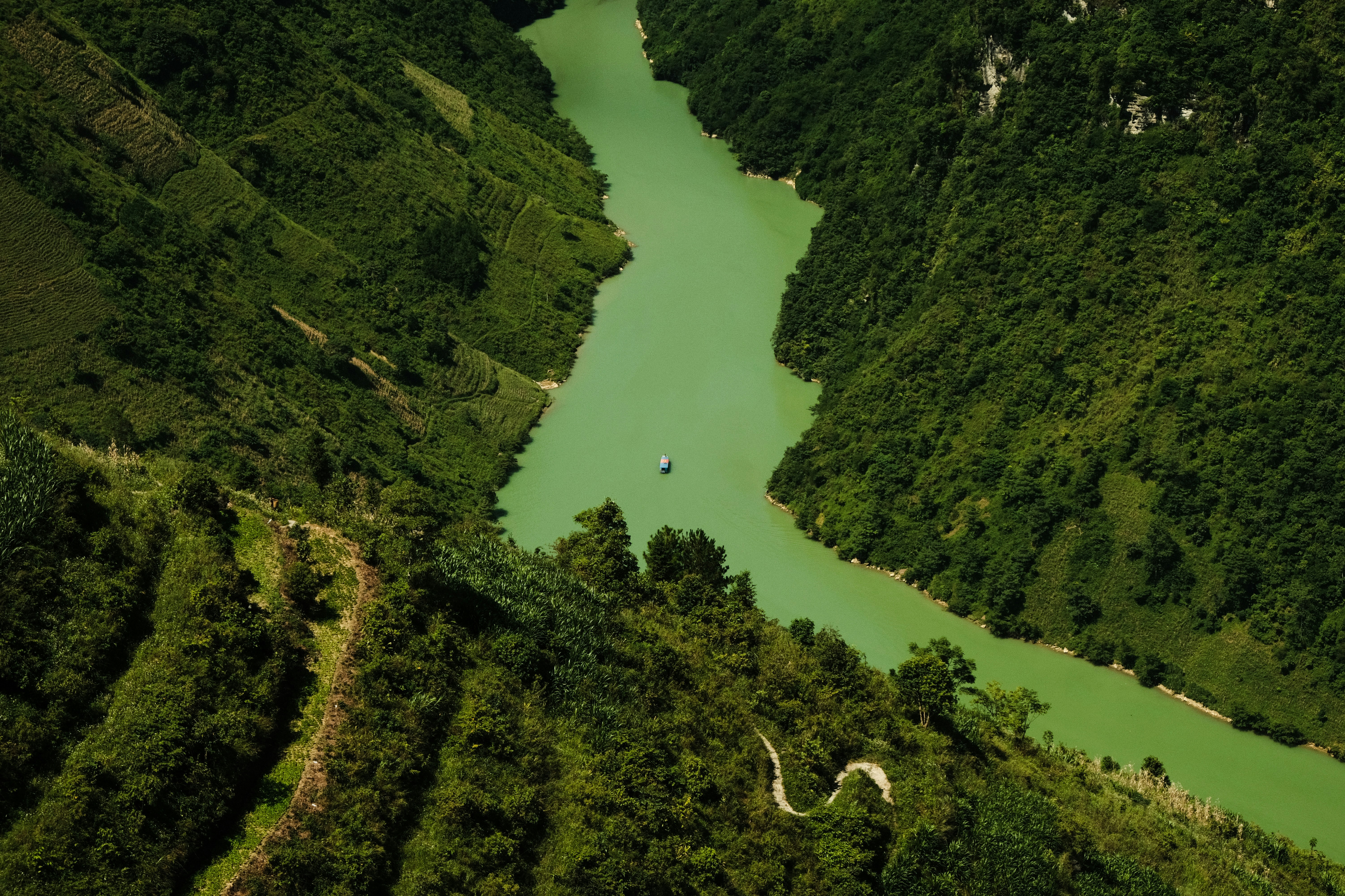 A small boat on a green river winding through steep forested mountain slopes