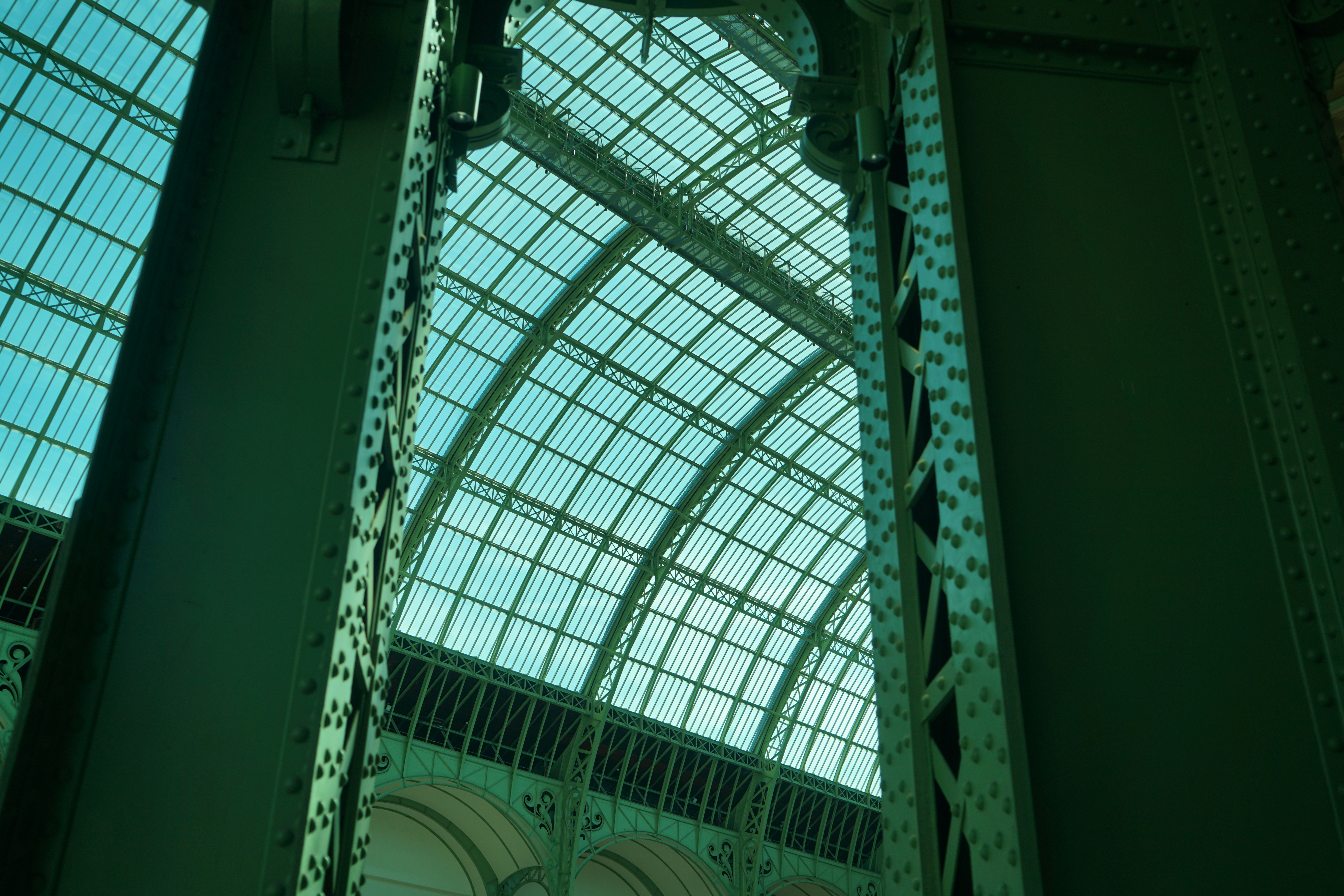 A vaulted glass ceiling framed by green metal girders in a large hall