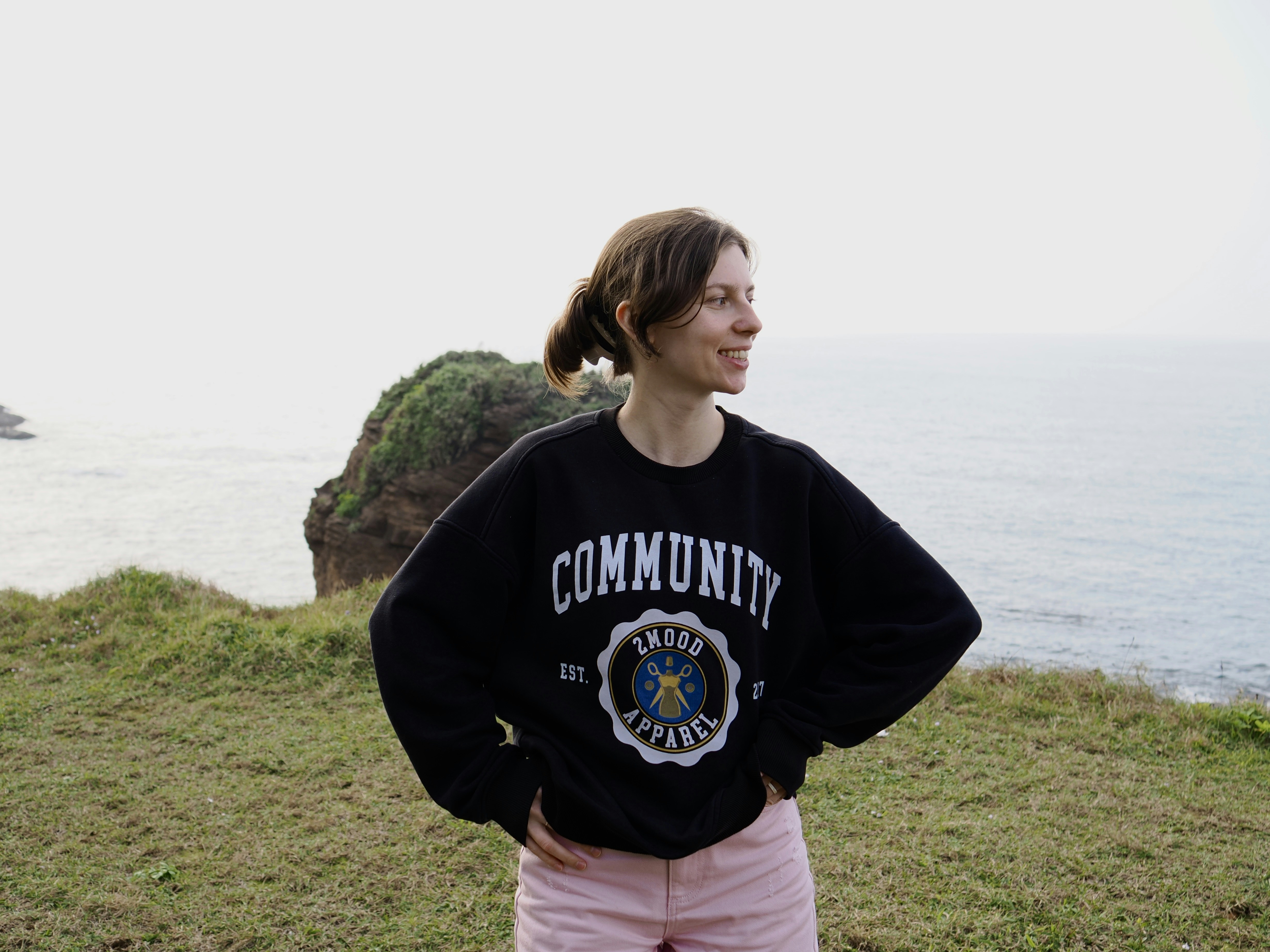 A woman in a black sweatshirt with hands on hips on a grassy cliff