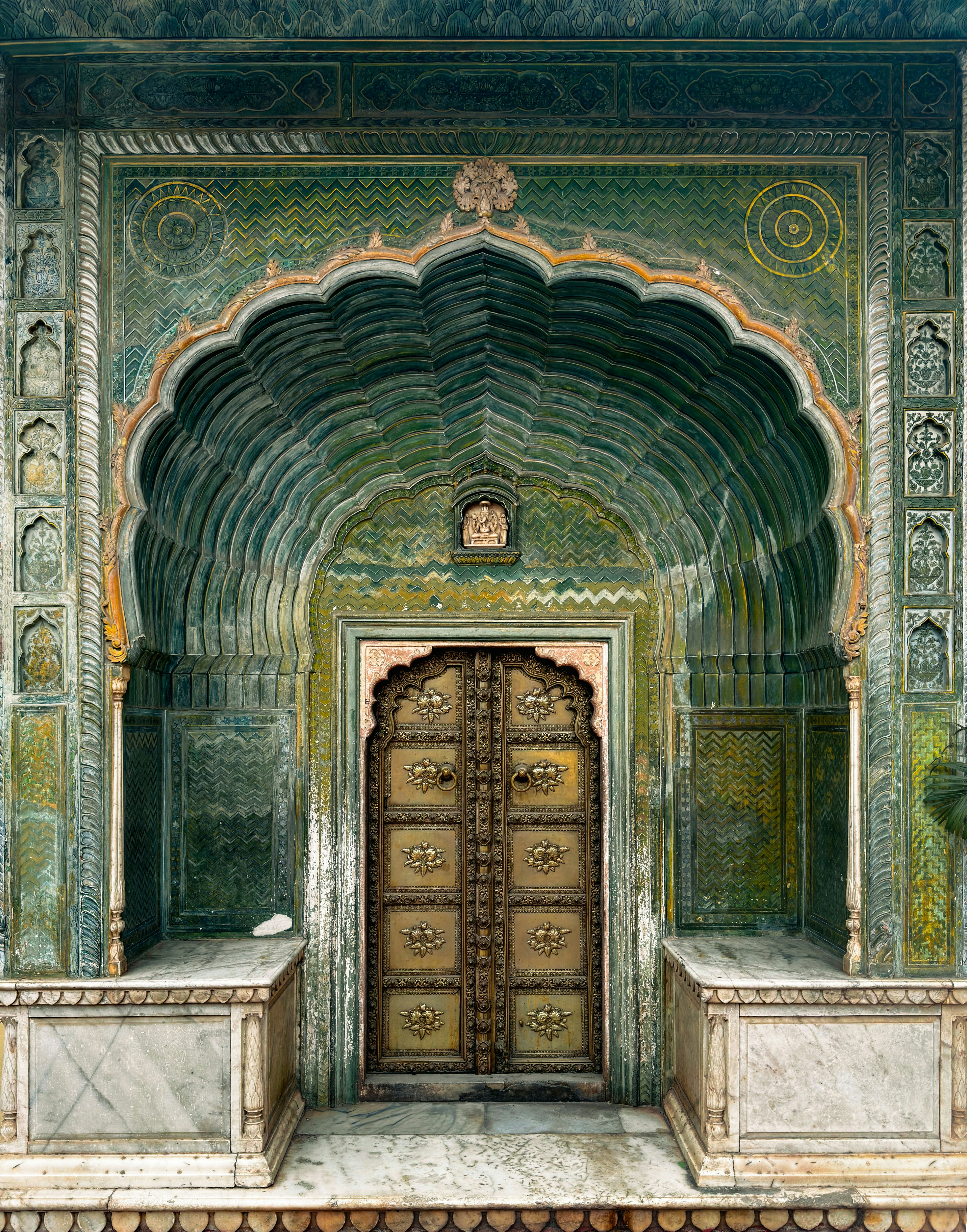An ornate brass door set within a green arched alcove with intricate carvings
