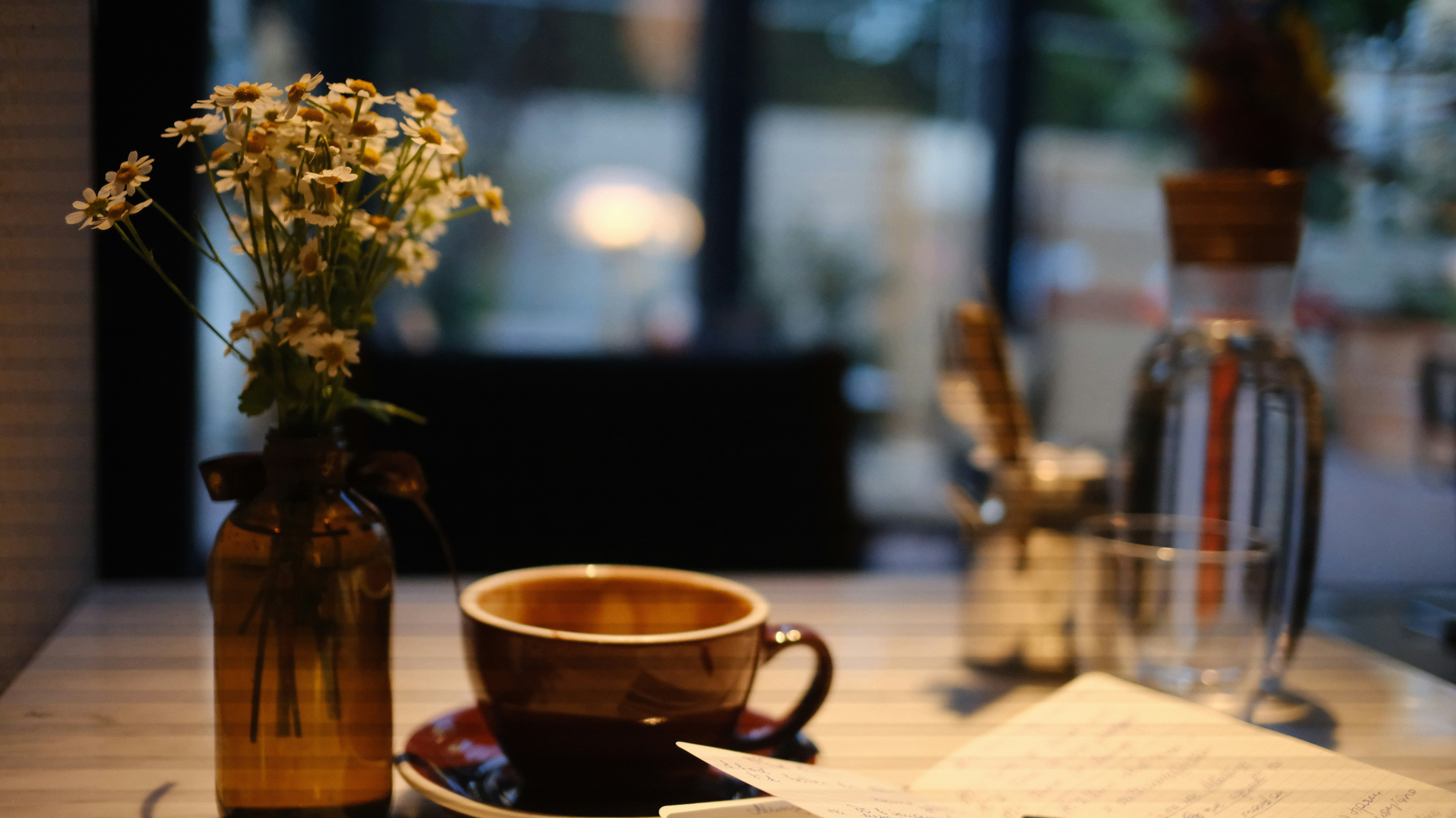 Cup of coffee beside a vase of daisies