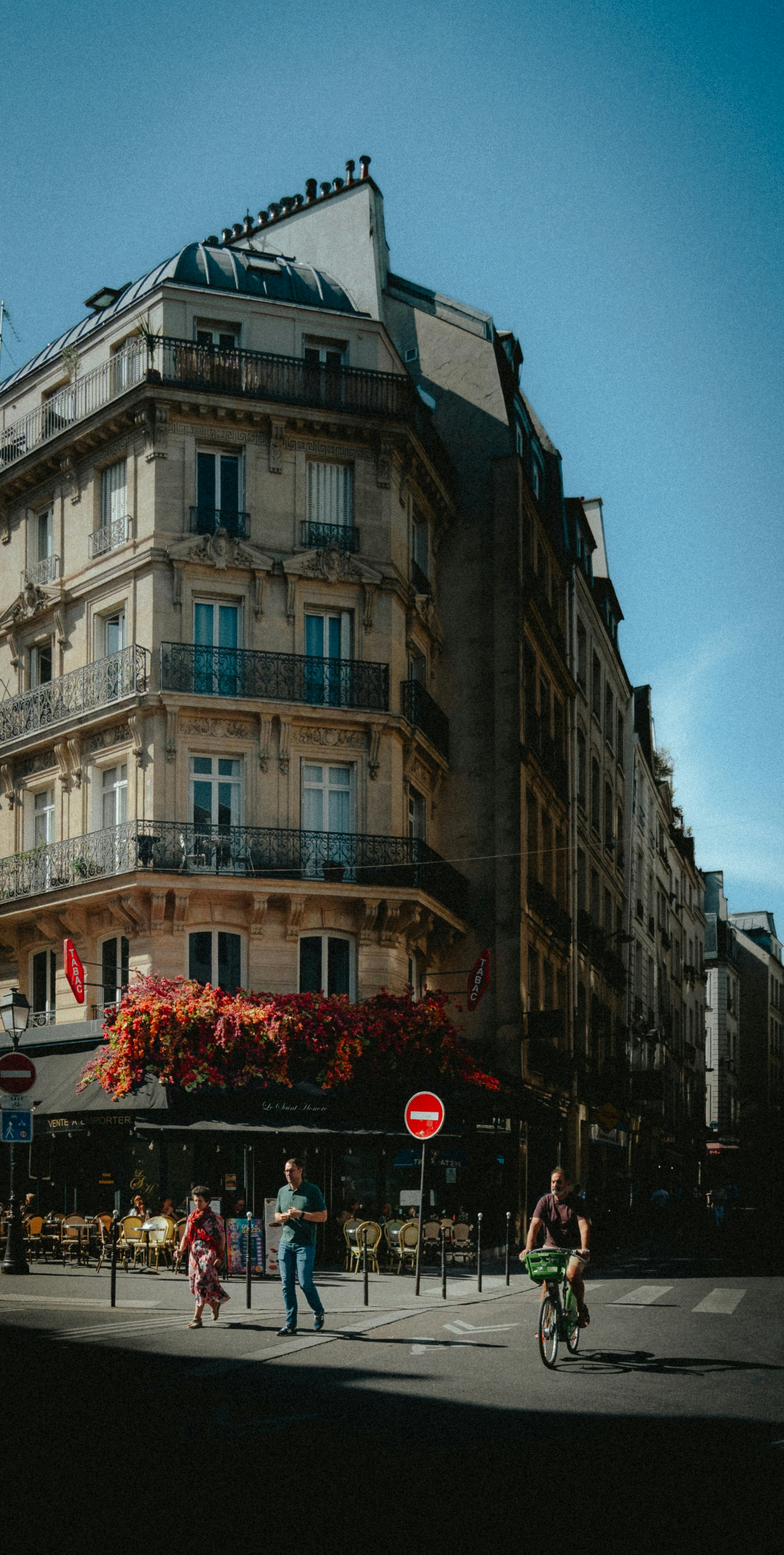 People walking and cycling past a corner cafe with flowers in Paris