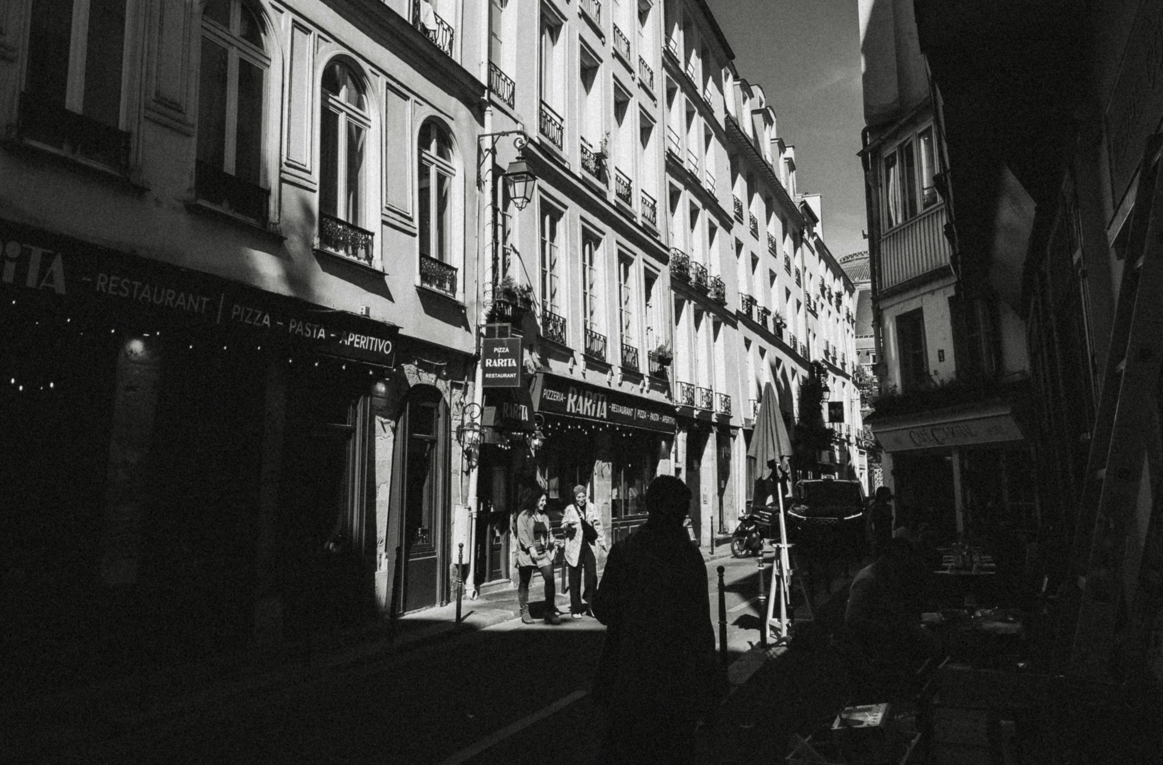 People walking along a narrow street lined with restaurants in Paris, France