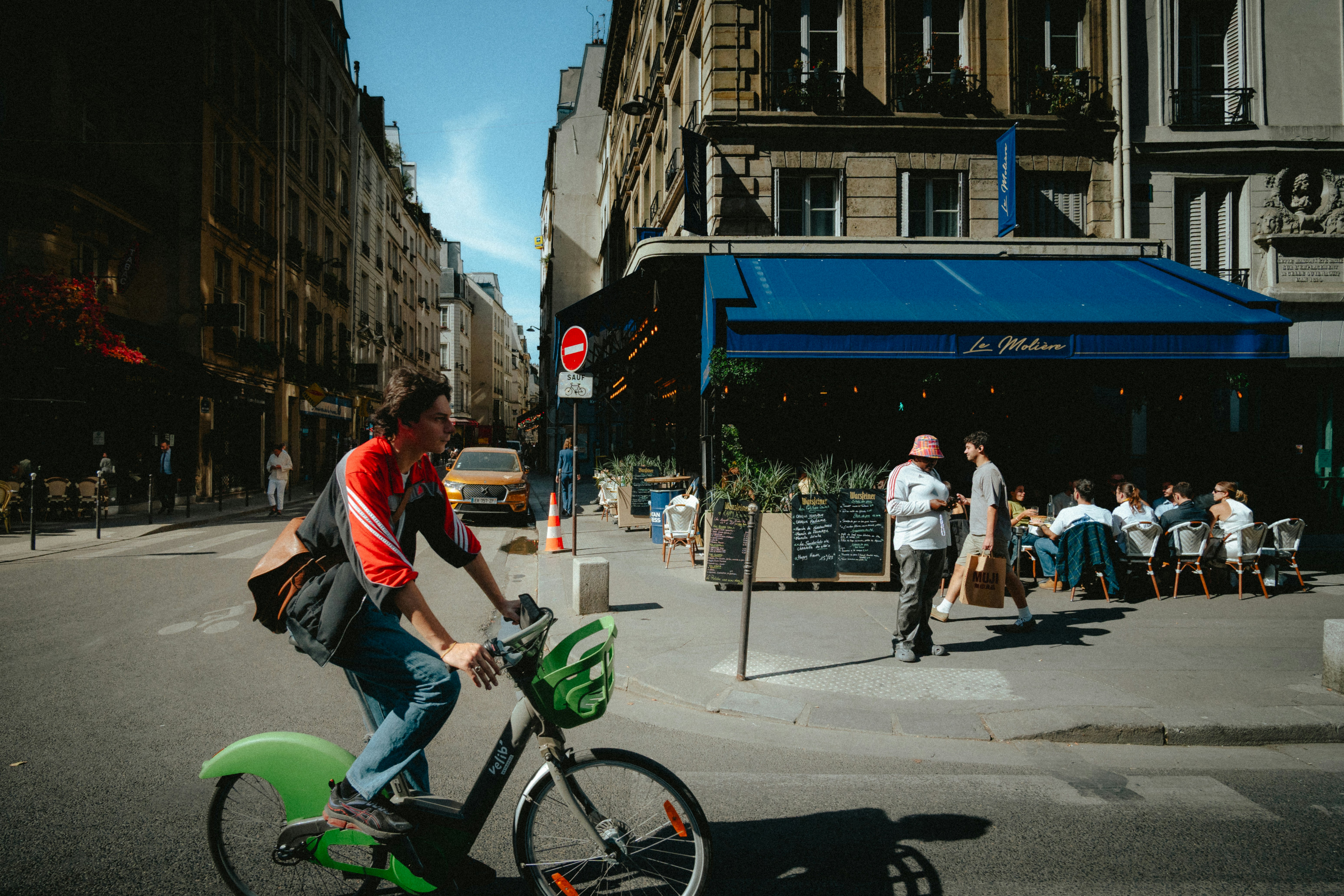 A person cycling a green bike past a cafe in Paris, France