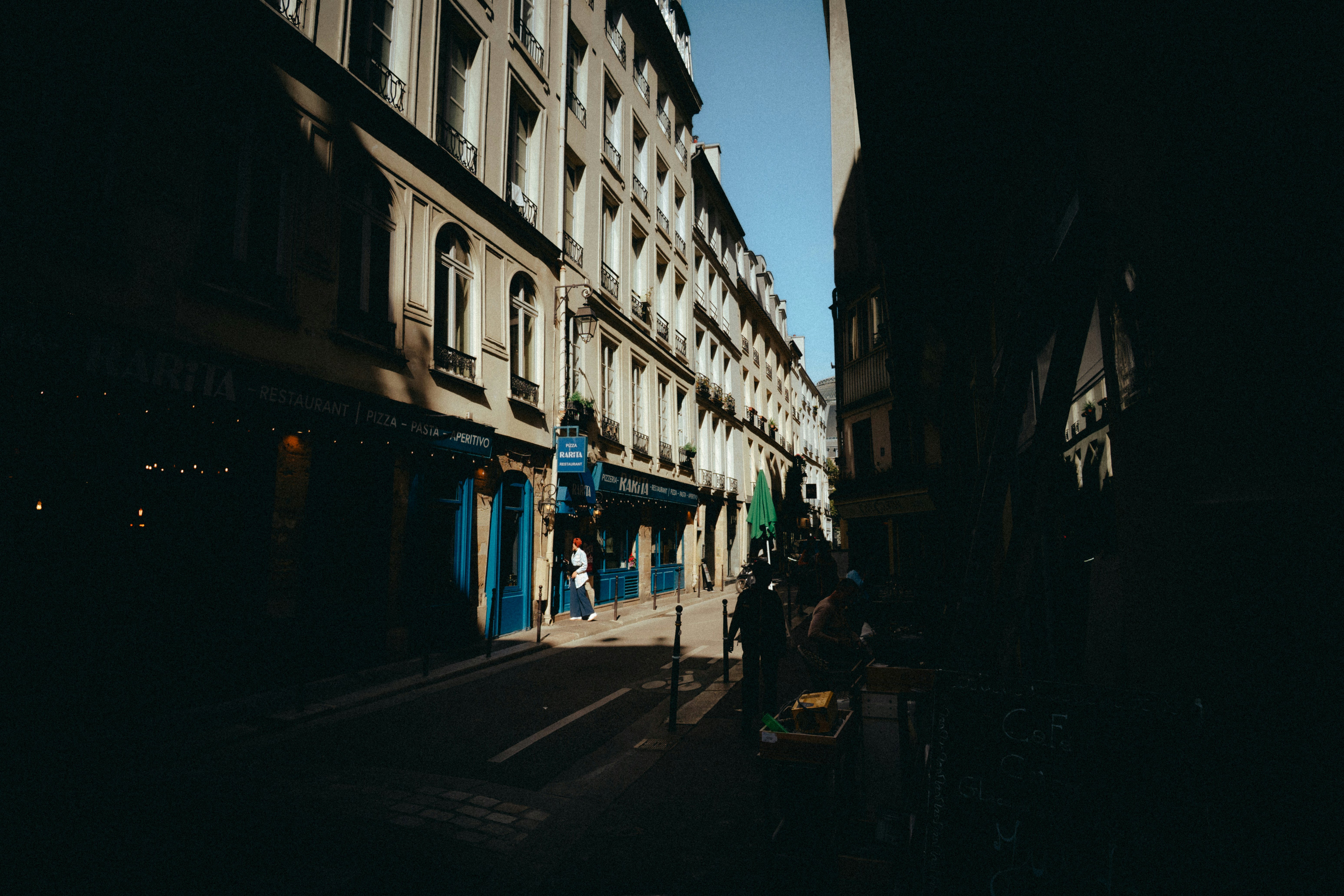 A narrow street with tall buildings and restaurant storefronts in Paris, France