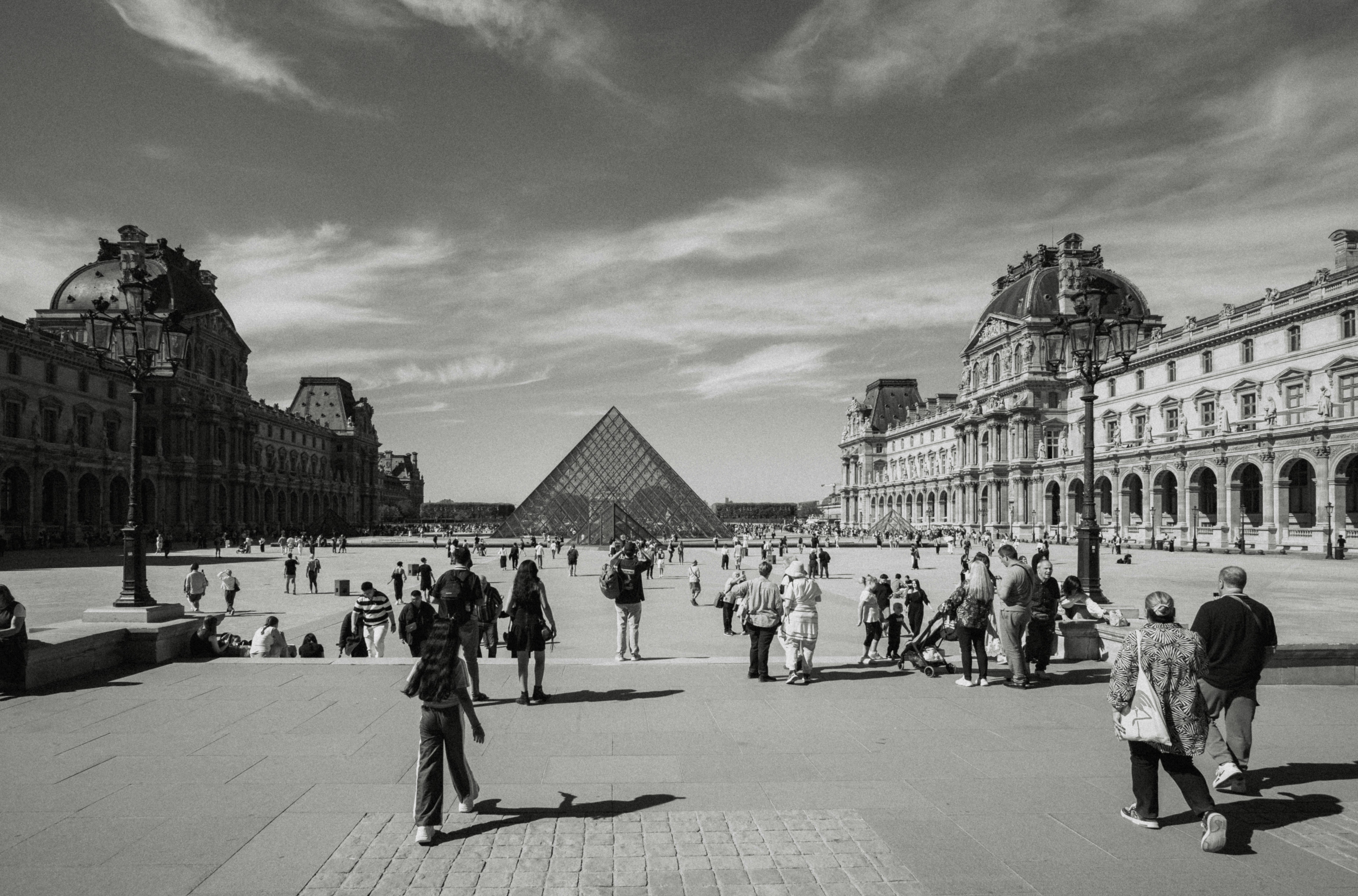 People walking in the Louvre courtyard with the glass pyramid in Paris