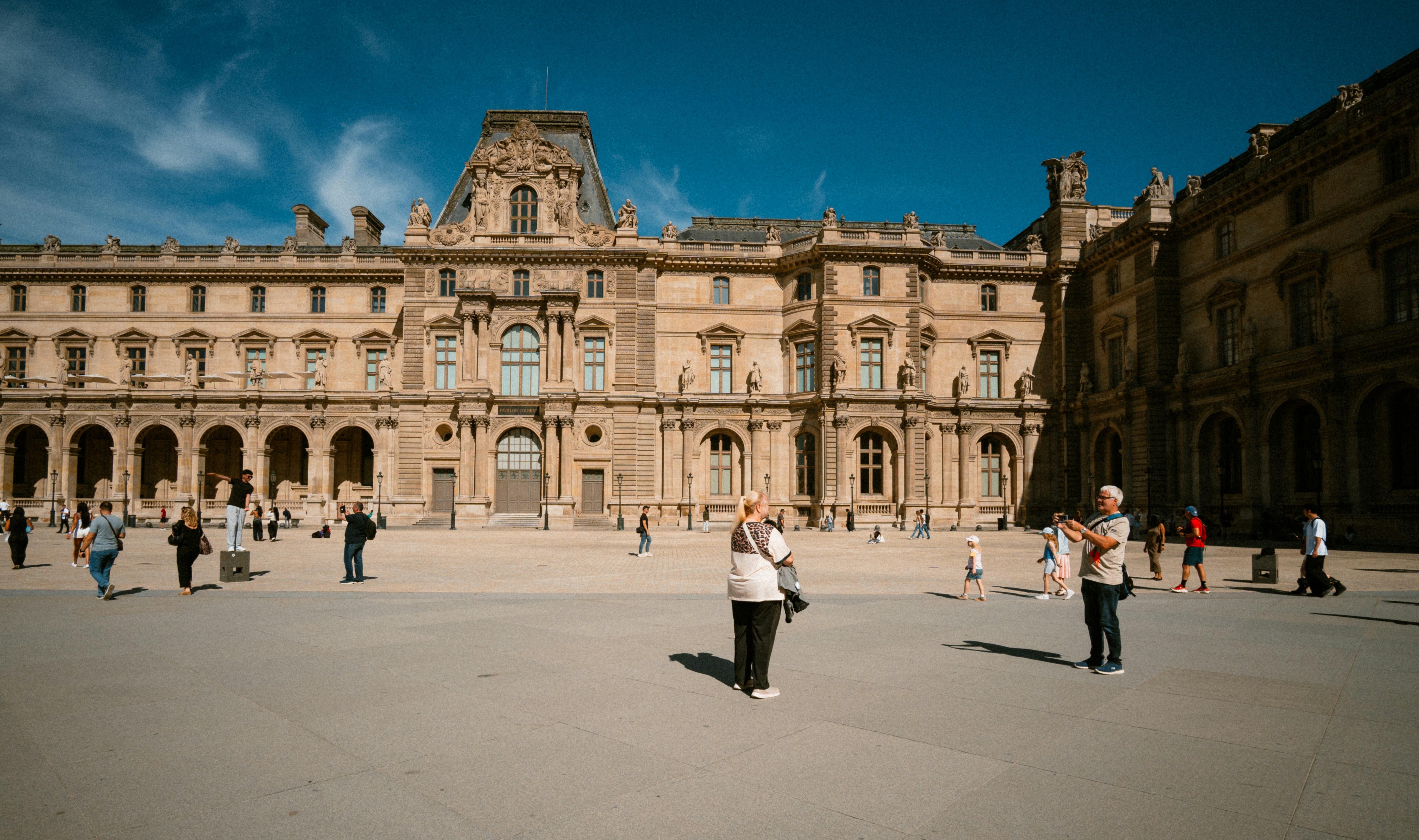 People walking and taking photos in the courtyard of the Louvre Museum in Paris