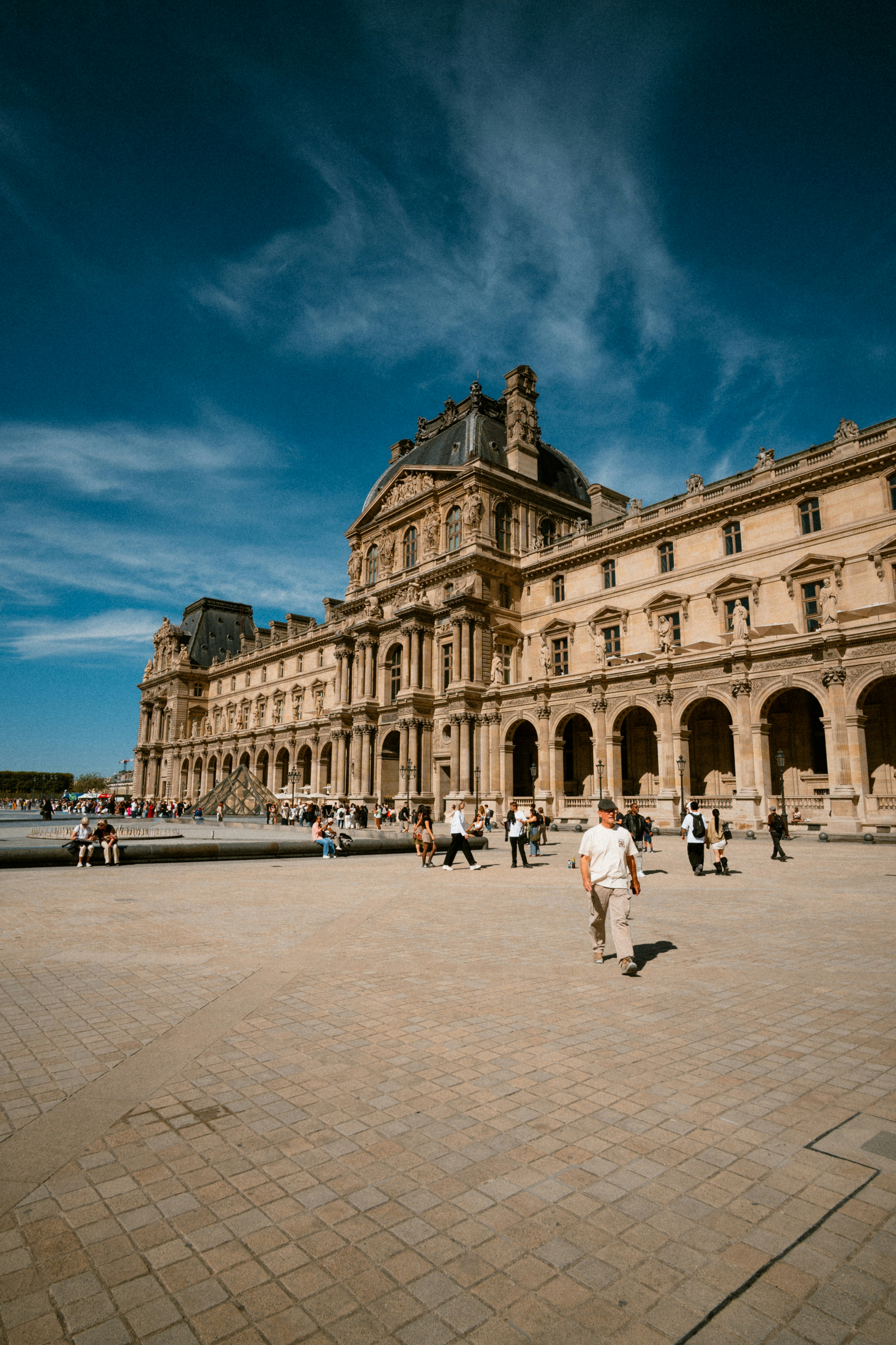 People walking in the courtyard of the Louvre Museum in Paris under blue skies