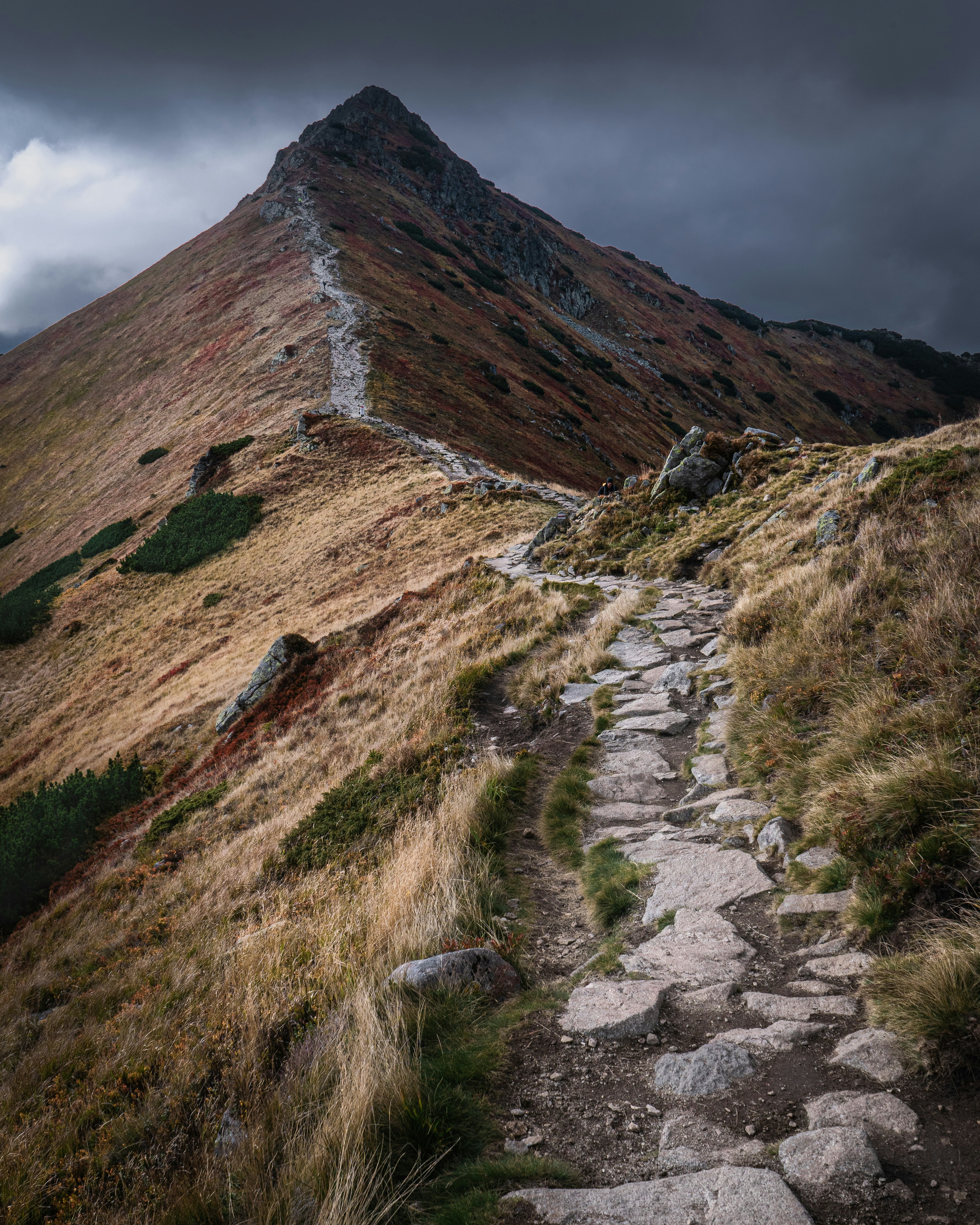 A stone hiking trail leading up a grassy mountain ridge under dark clouds