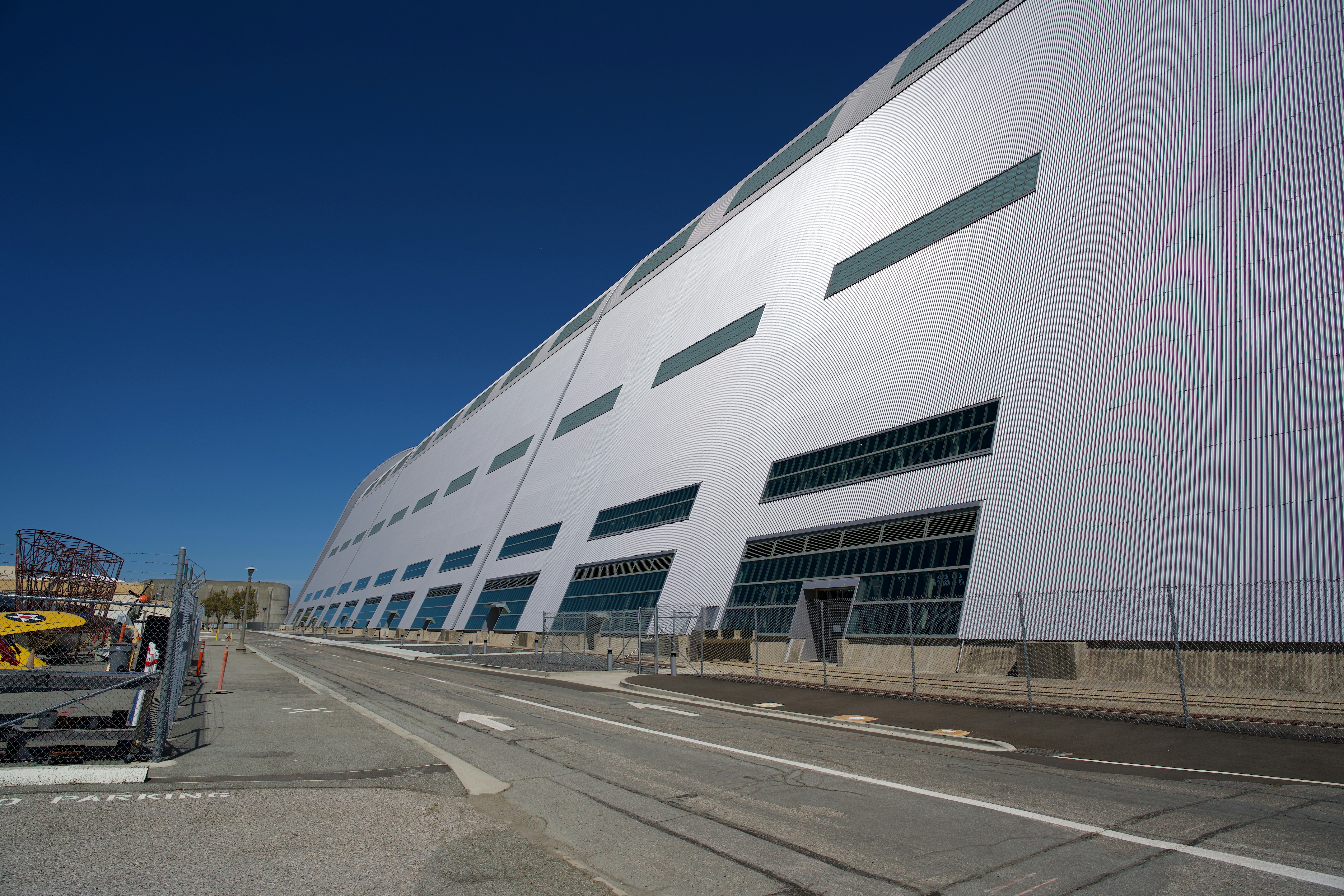A massive silver industrial building with horizontal windows beside a paved road