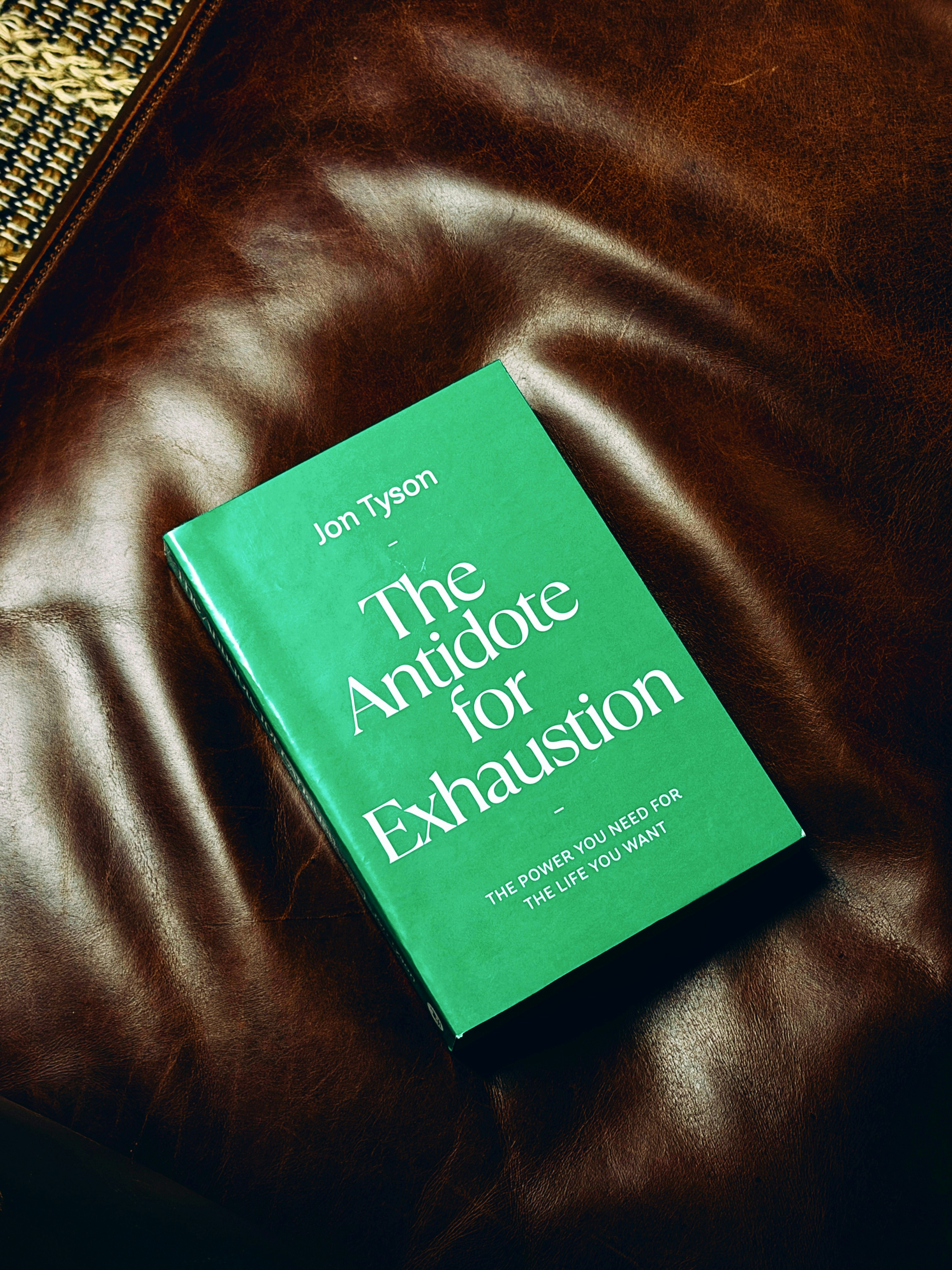 A green book titled The Antidote for Exhaustion on a brown leather surface