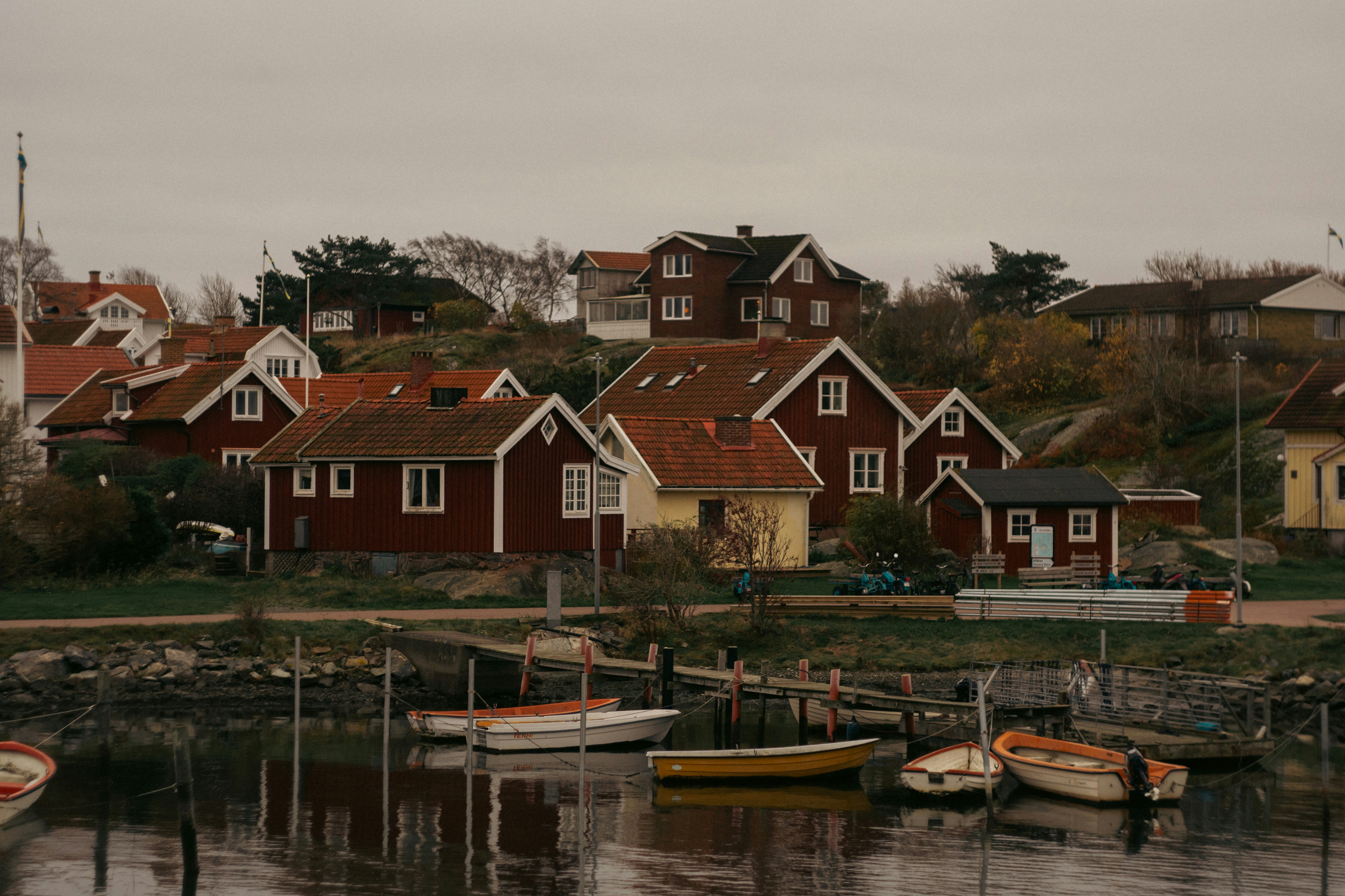 Small boats moored at a wooden pier below red houses on a rocky coast