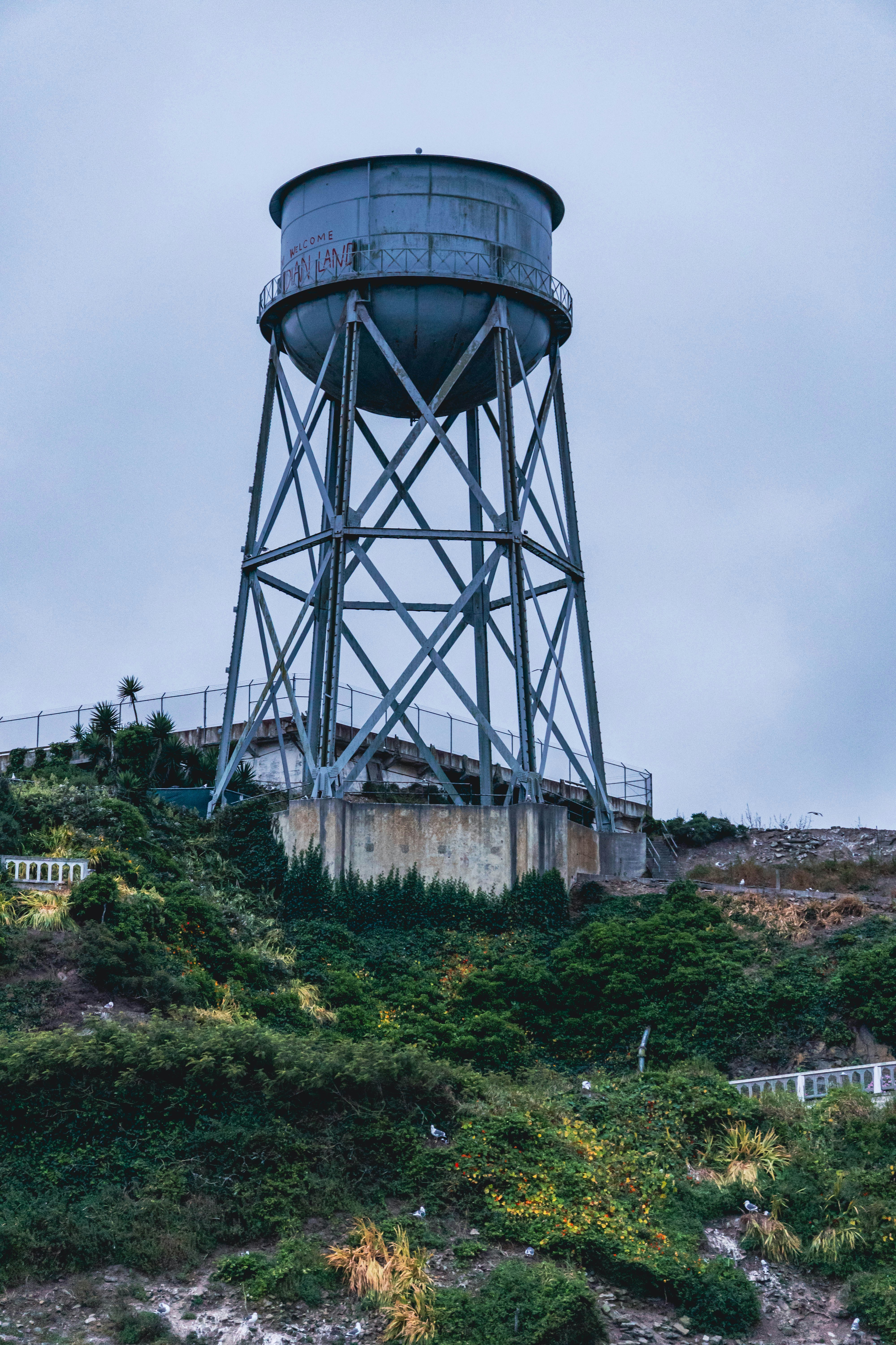 A large metal water tower on a hillside covered in green vegetation