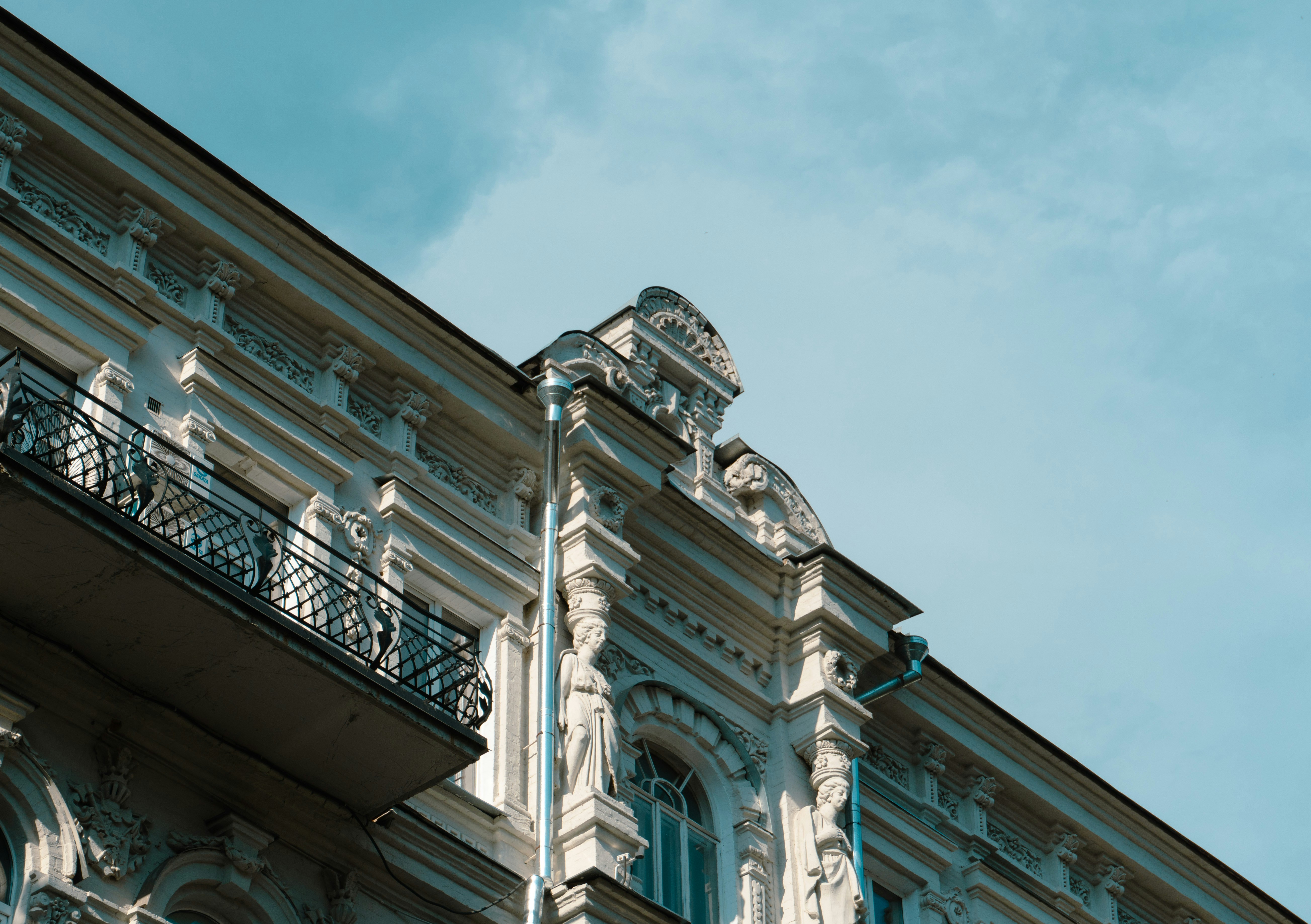 Ornate white building facade with classical statues and a black iron balcony
