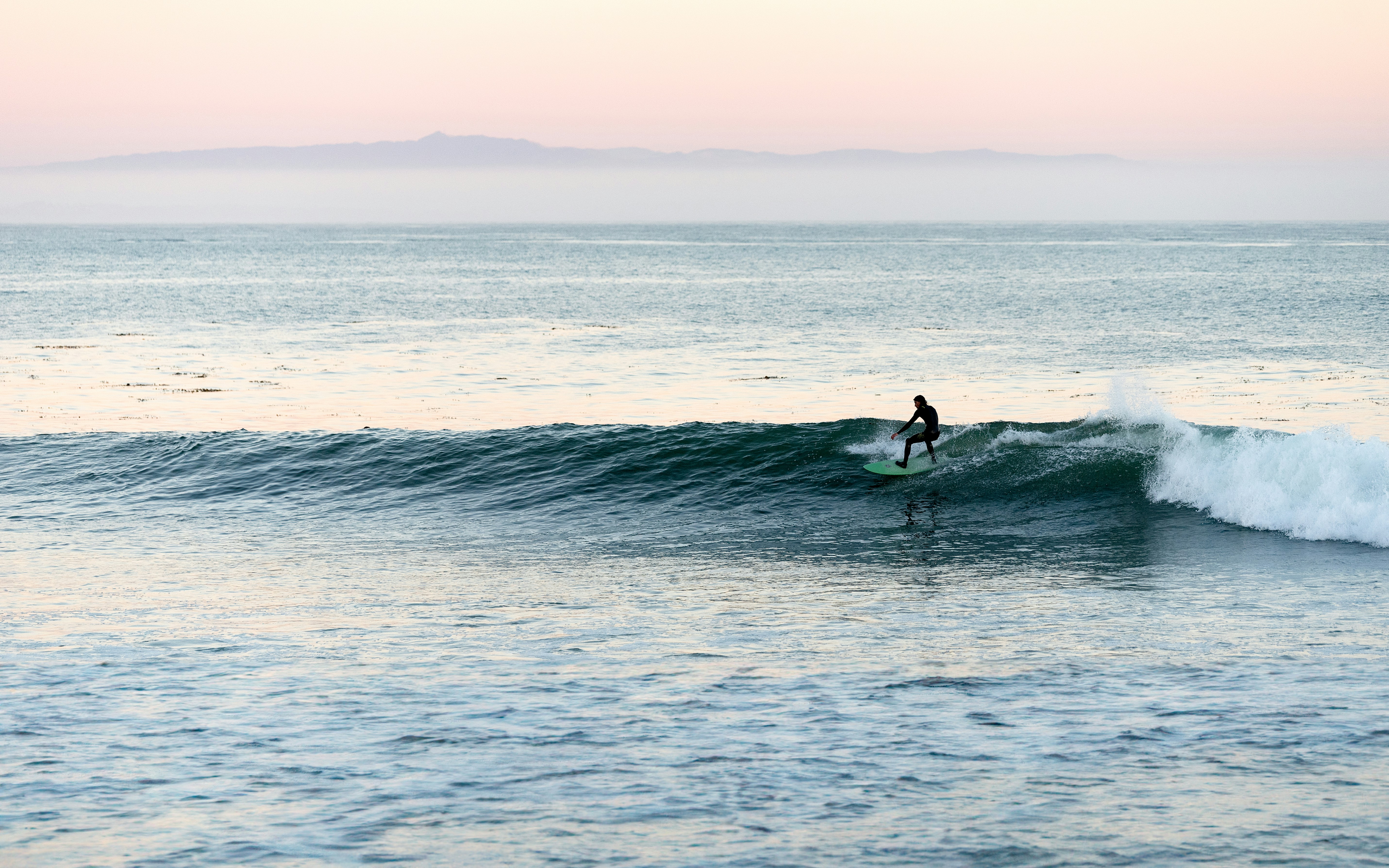 A surfer riding a wave in the ocean under a soft pale sky