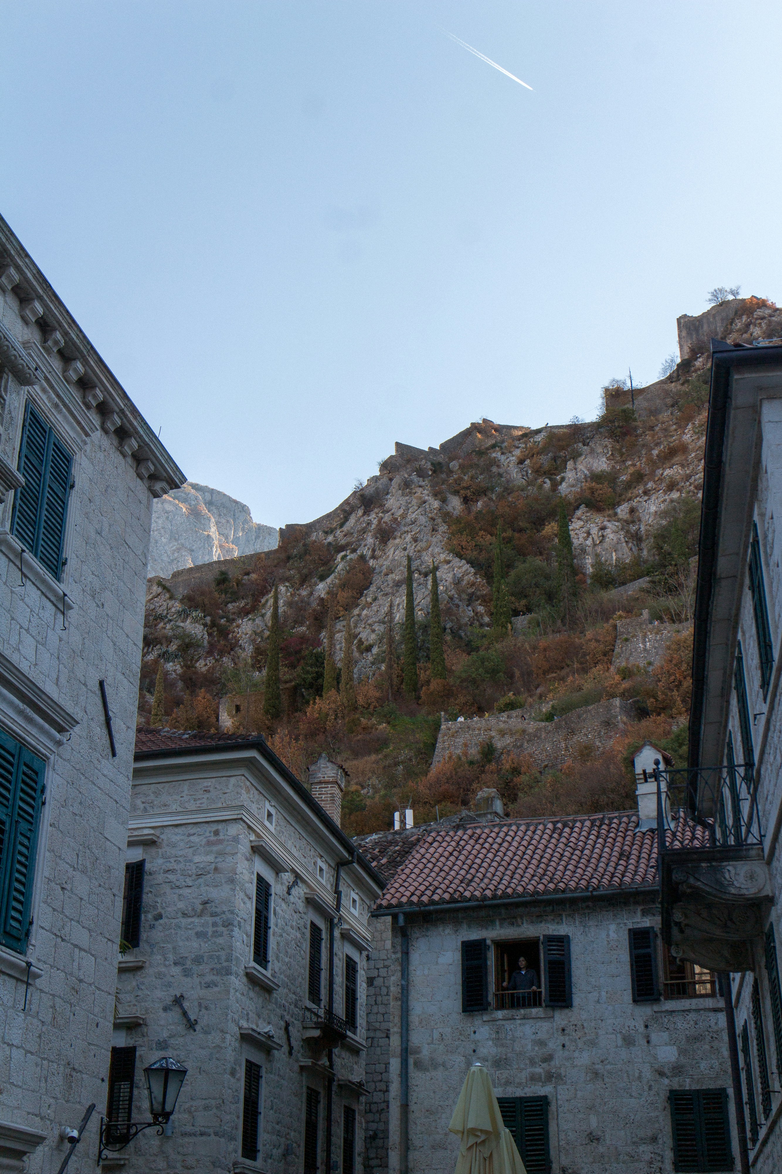 Stone buildings with green shutters below a steep rocky mountain in Kotor