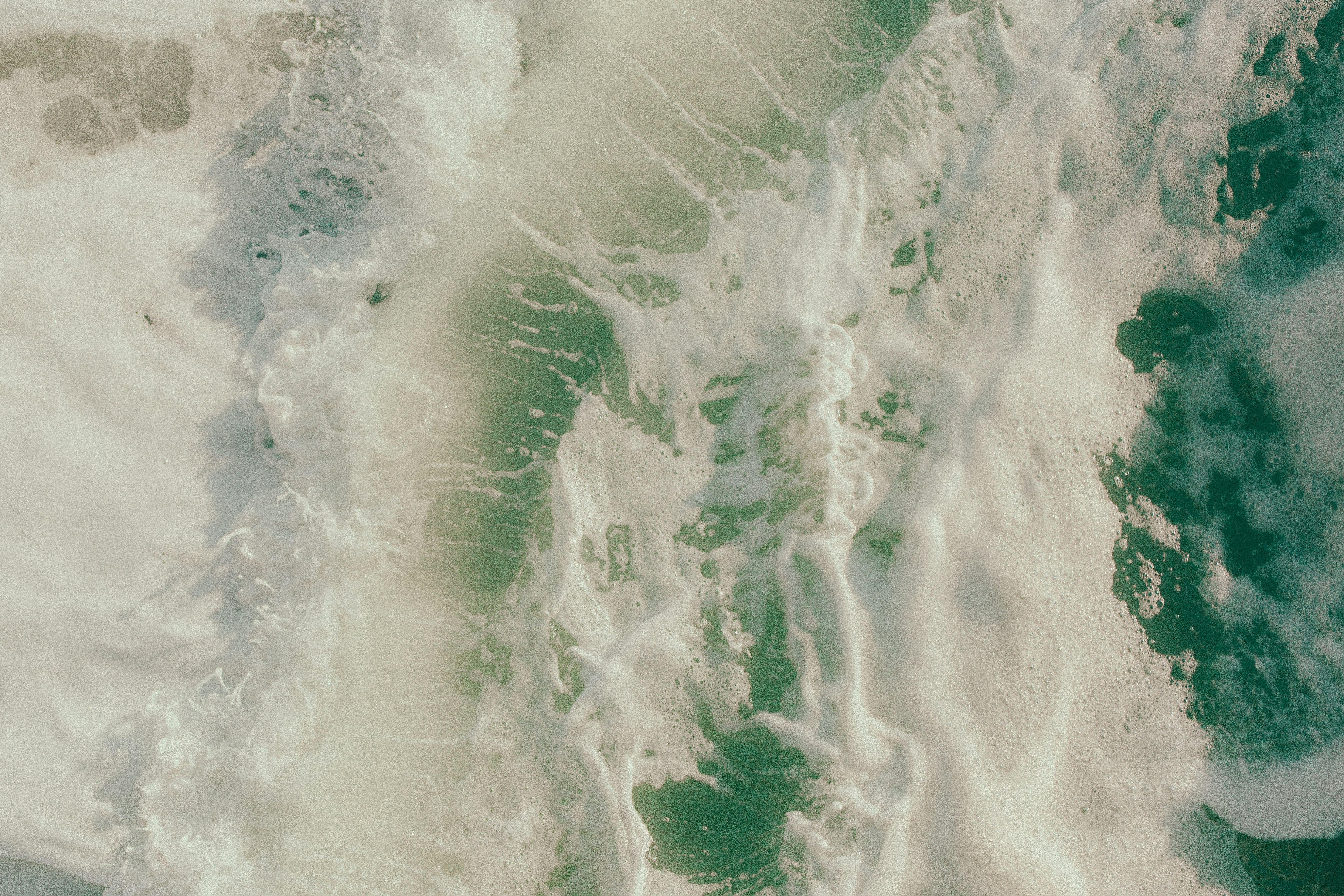 Aerial view of white sea foam swirling over turquoise ocean water