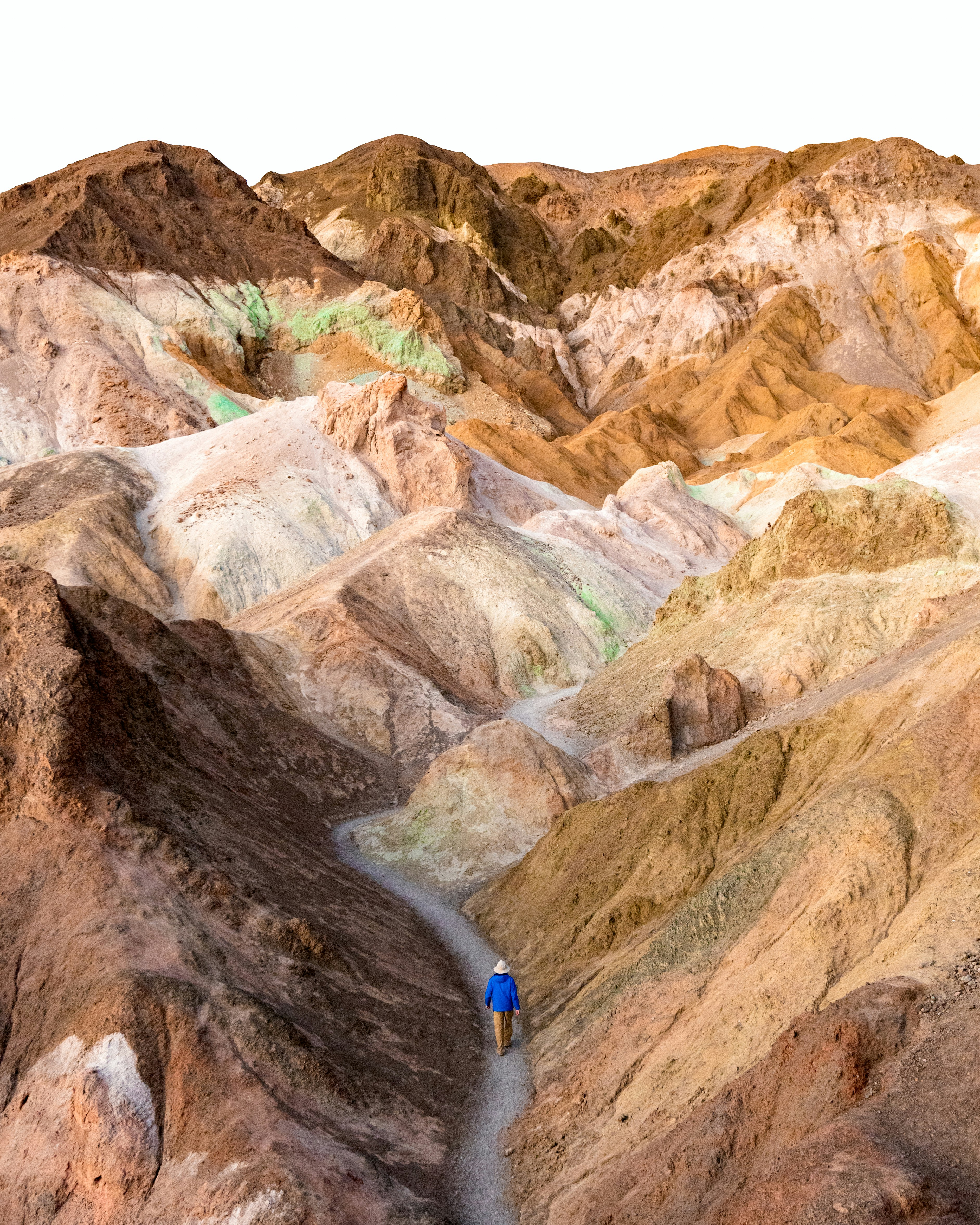 A person in a blue jacket walking along a trail through colorful desert hills