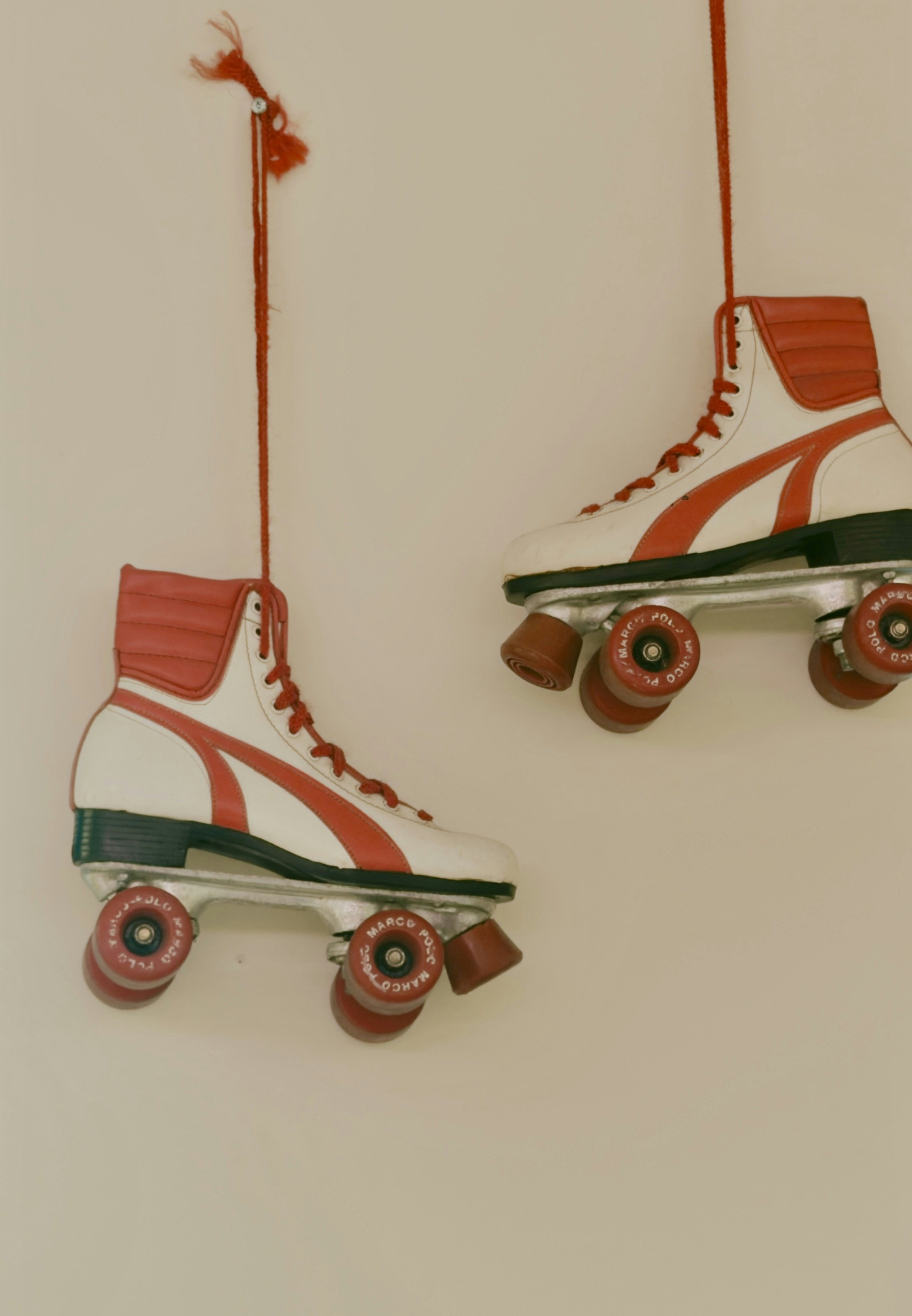 Two white and red roller skates hanging by red laces against a plain wall