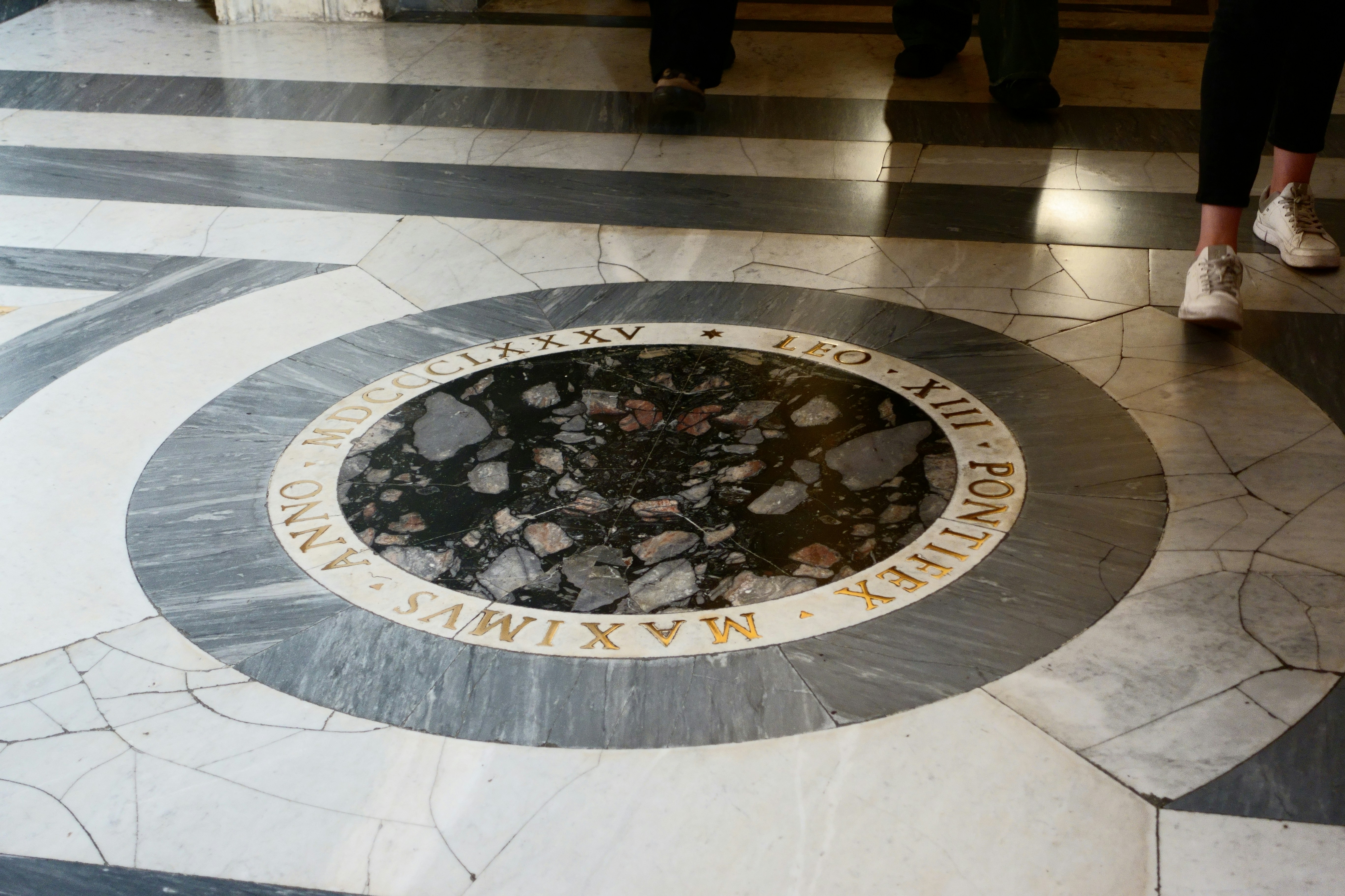 A circular marble floor inlay with gold lettering and dark stone fragments