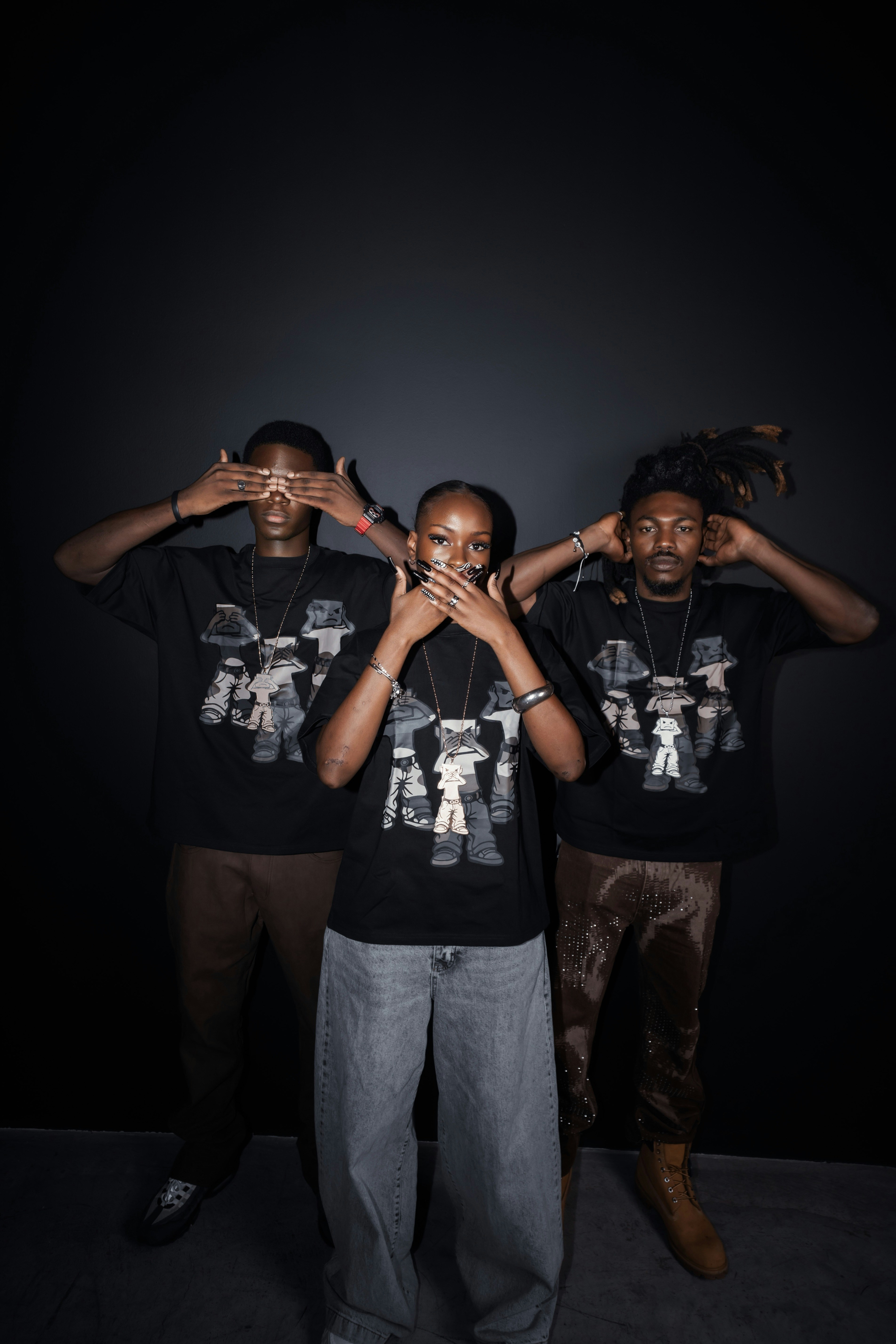 Three people in matching black graphic t-shirts posing against a dark background