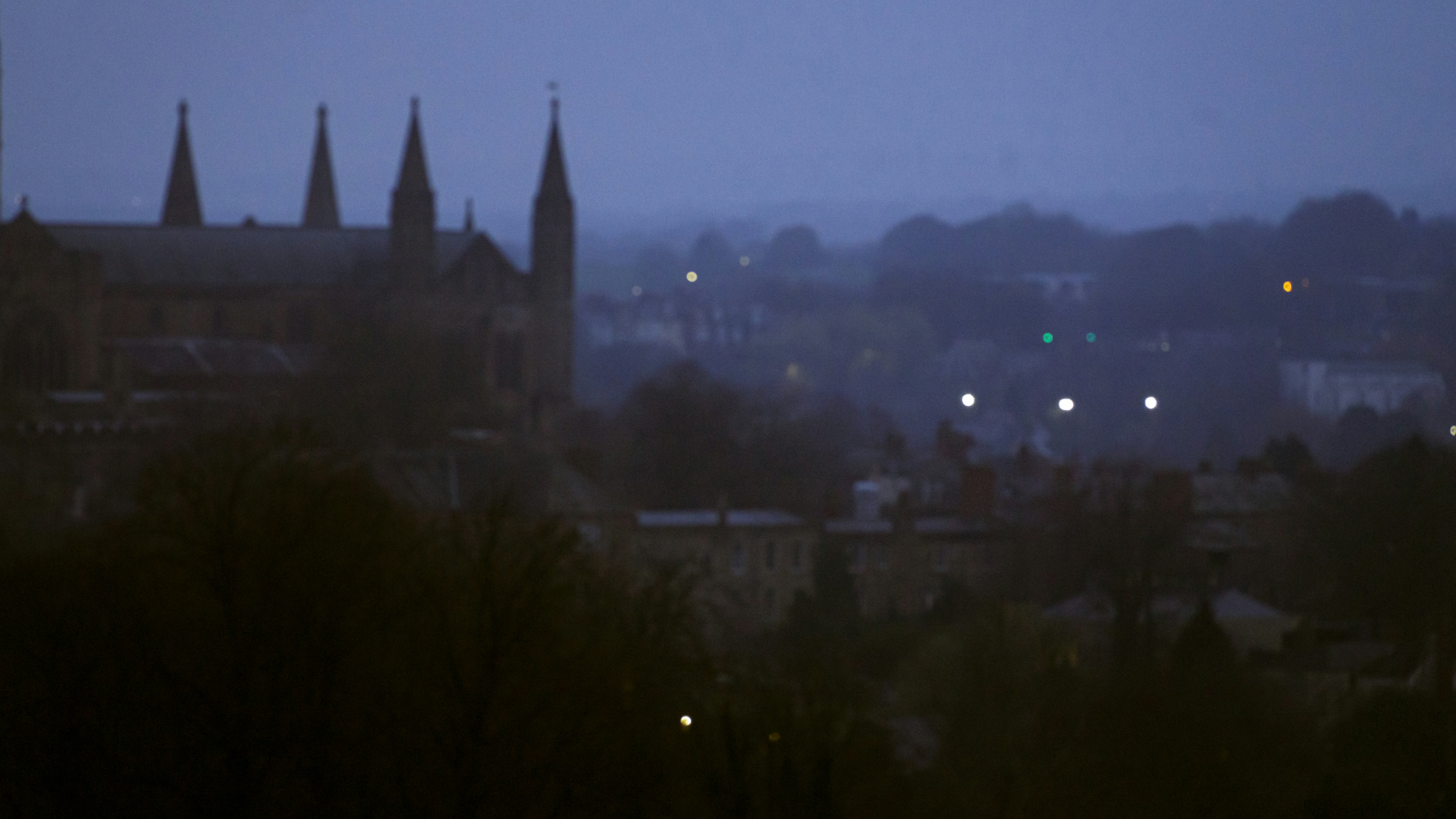 A gothic cathedral with tall spires overlooking a town at blue hour