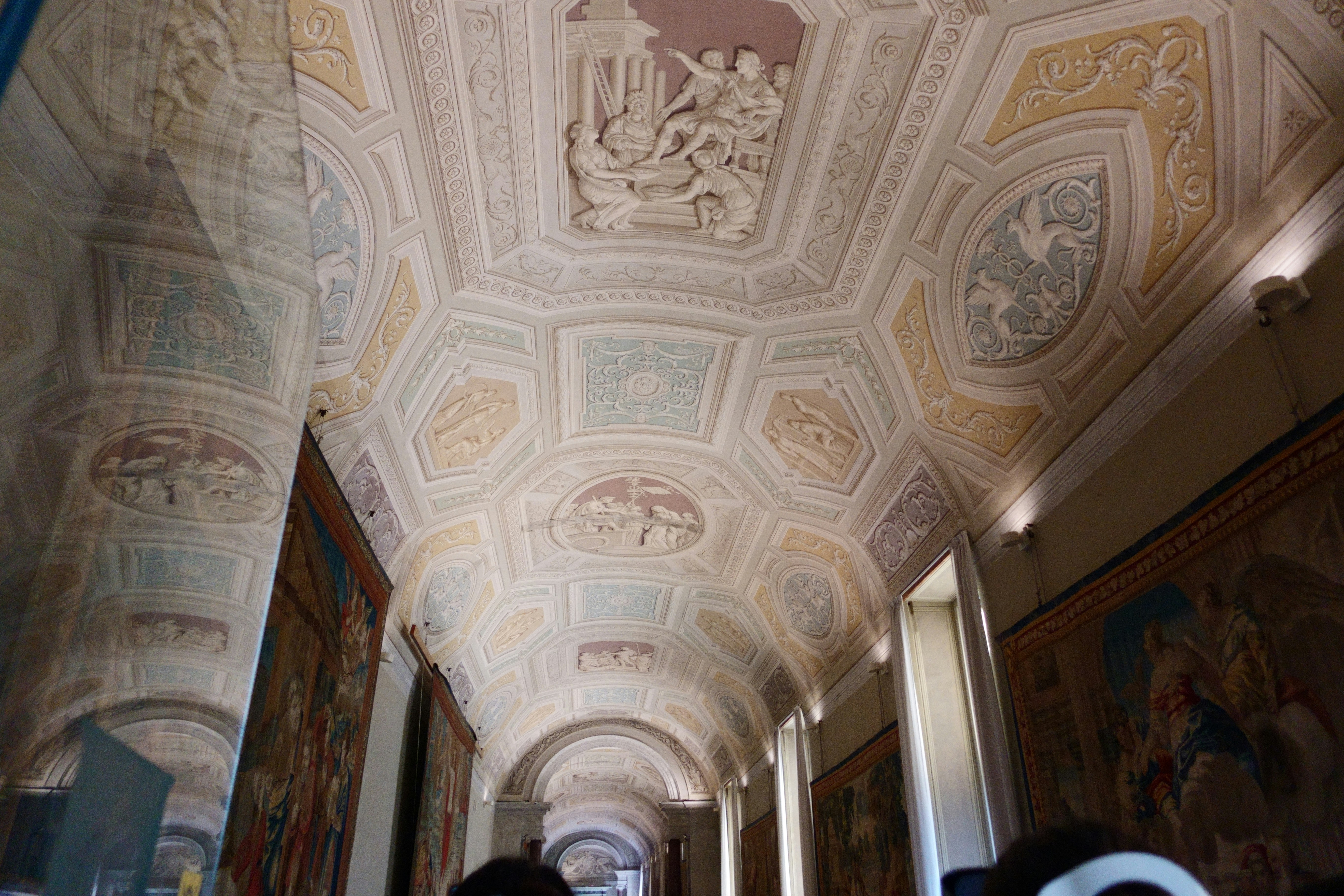An ornate vaulted ceiling with classical relief sculptures and tapestries lining the walls