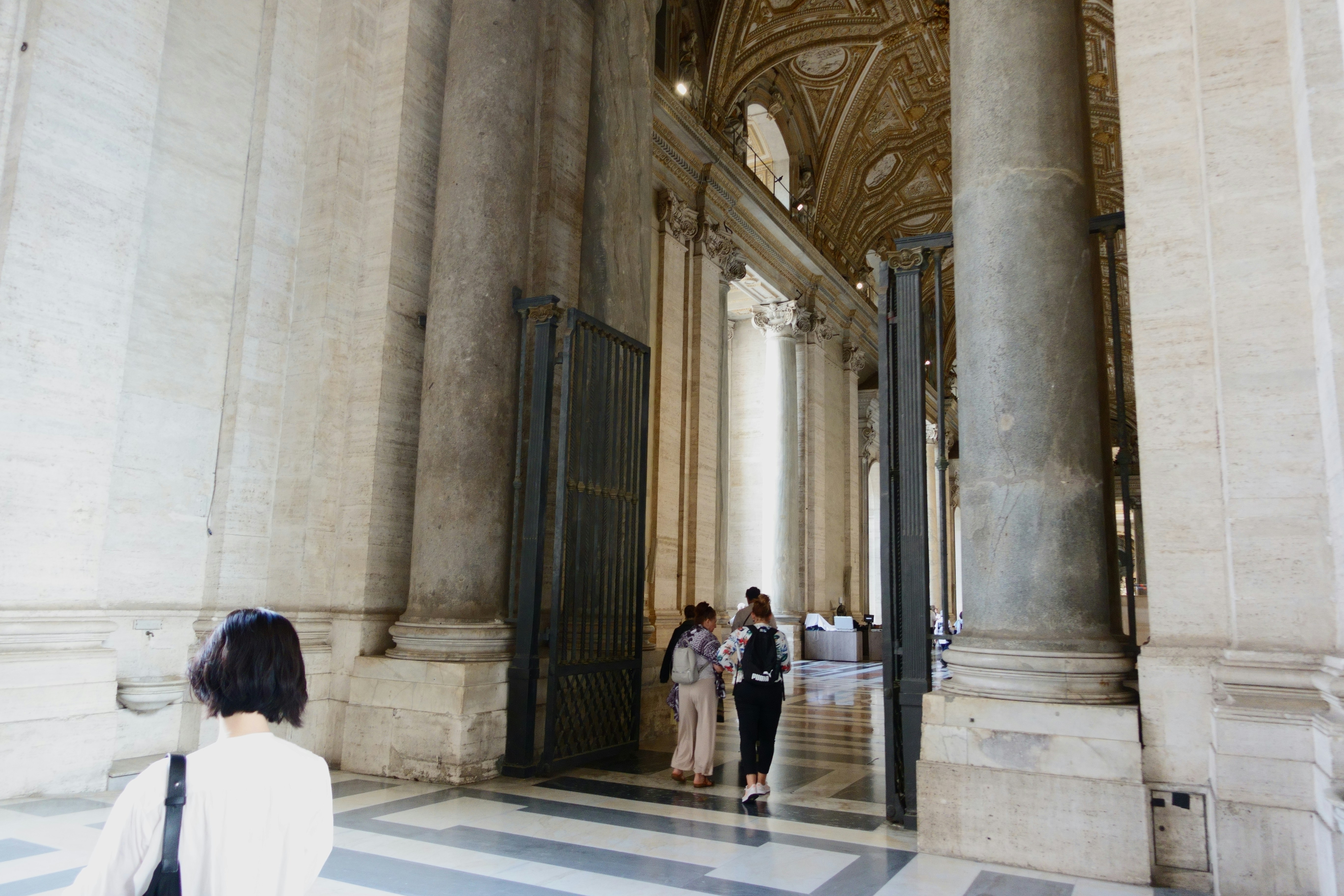 People walking through a grand stone archway with tall columns in St. Peter's Basilica