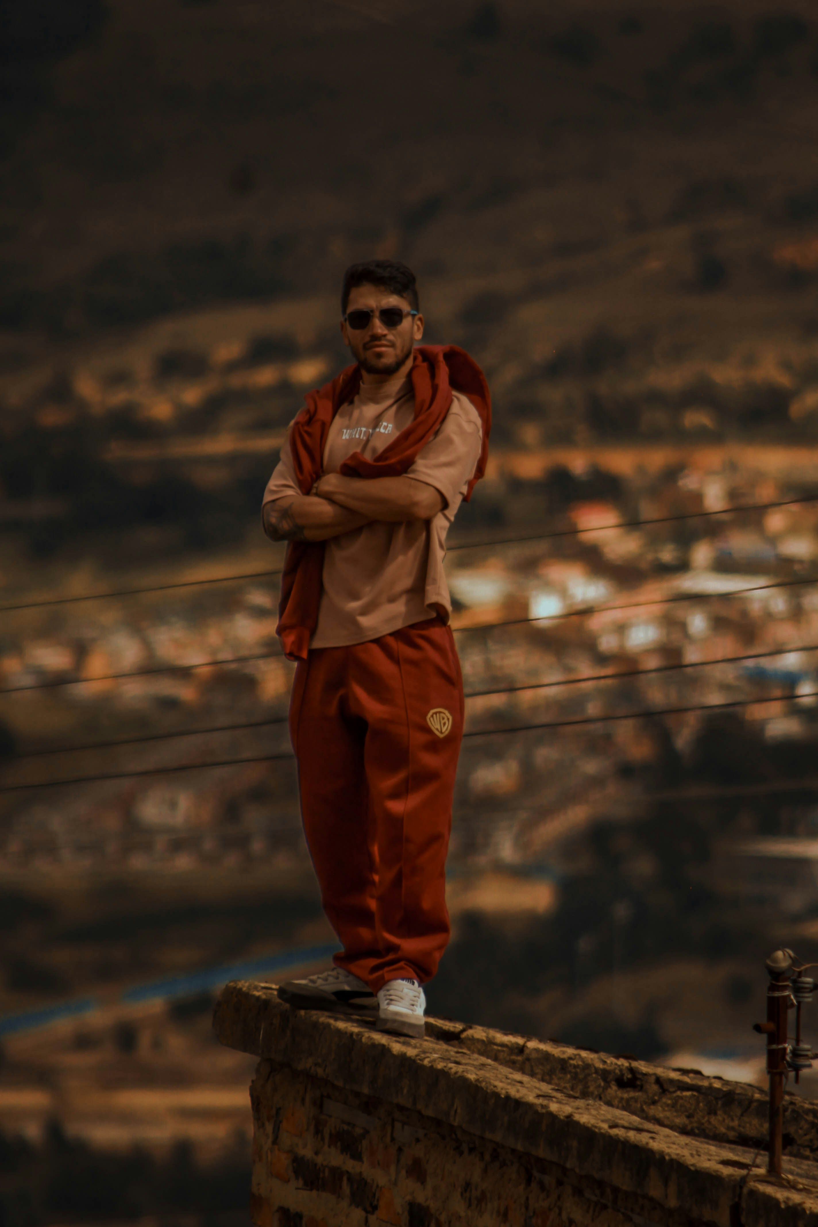 A man in sunglasses and a red tracksuit on a stone wall overlooking a town