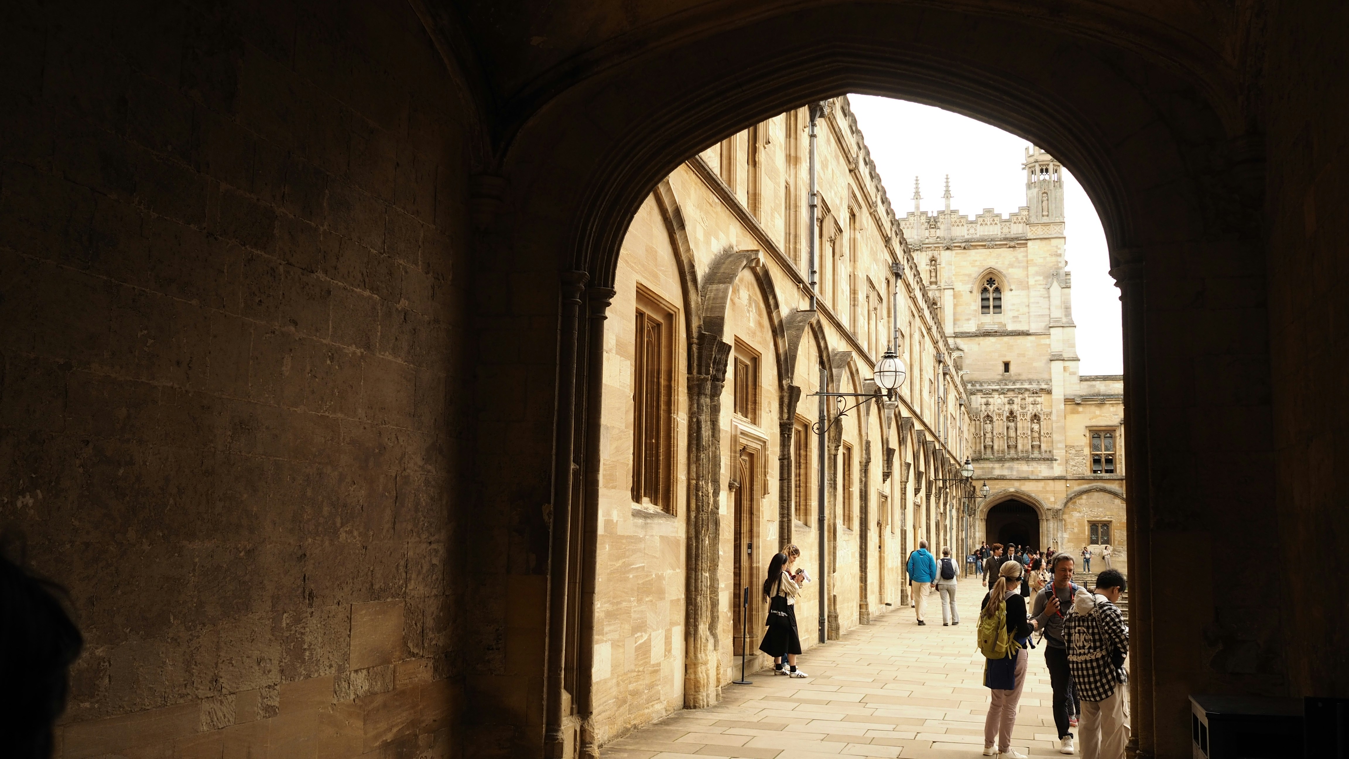 People walking through a stone archway into a sunlit courtyard of an old college - schoolhouse and education history