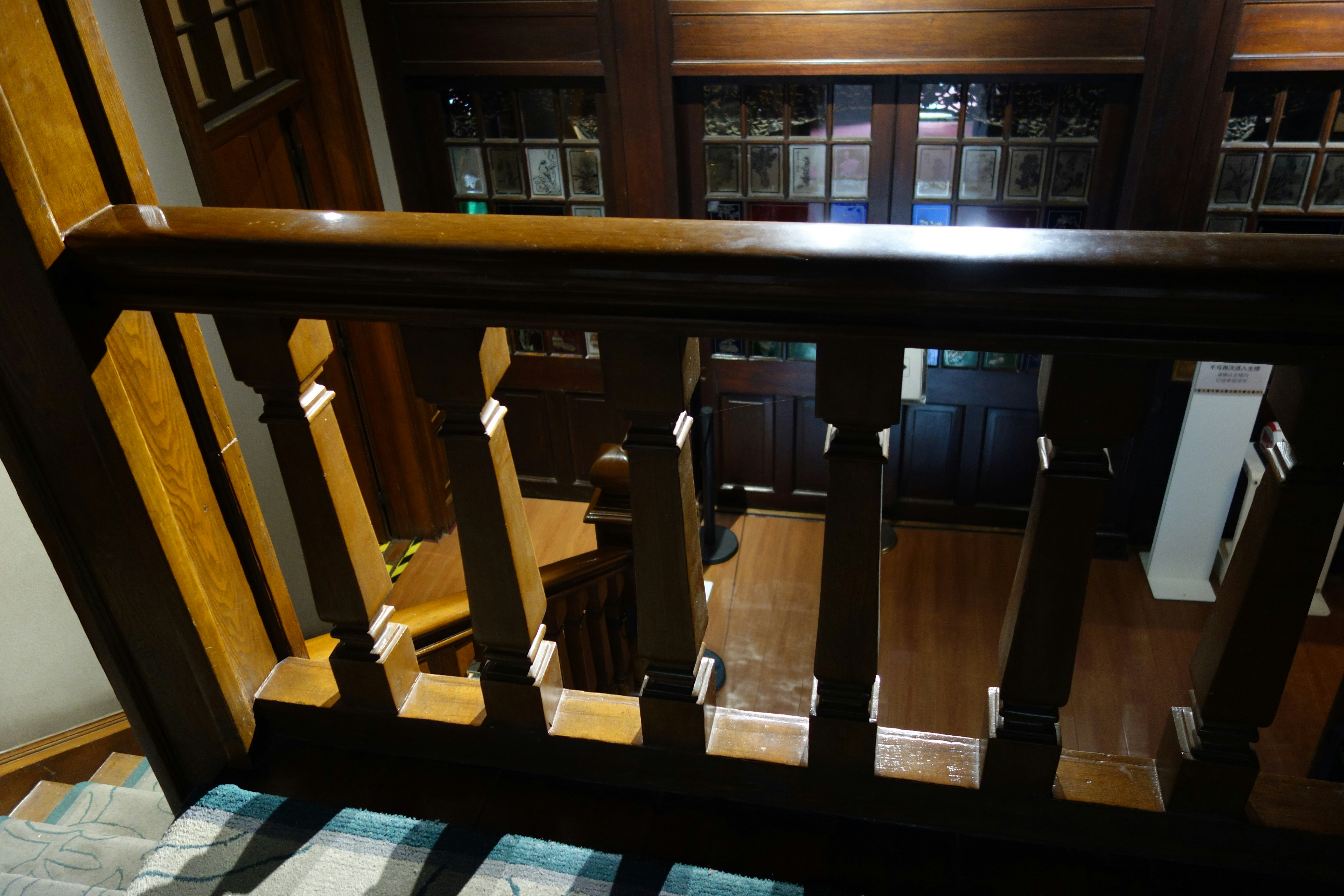 A dark wooden staircase railing looking down onto a landing with leaded glass doors in an old house.