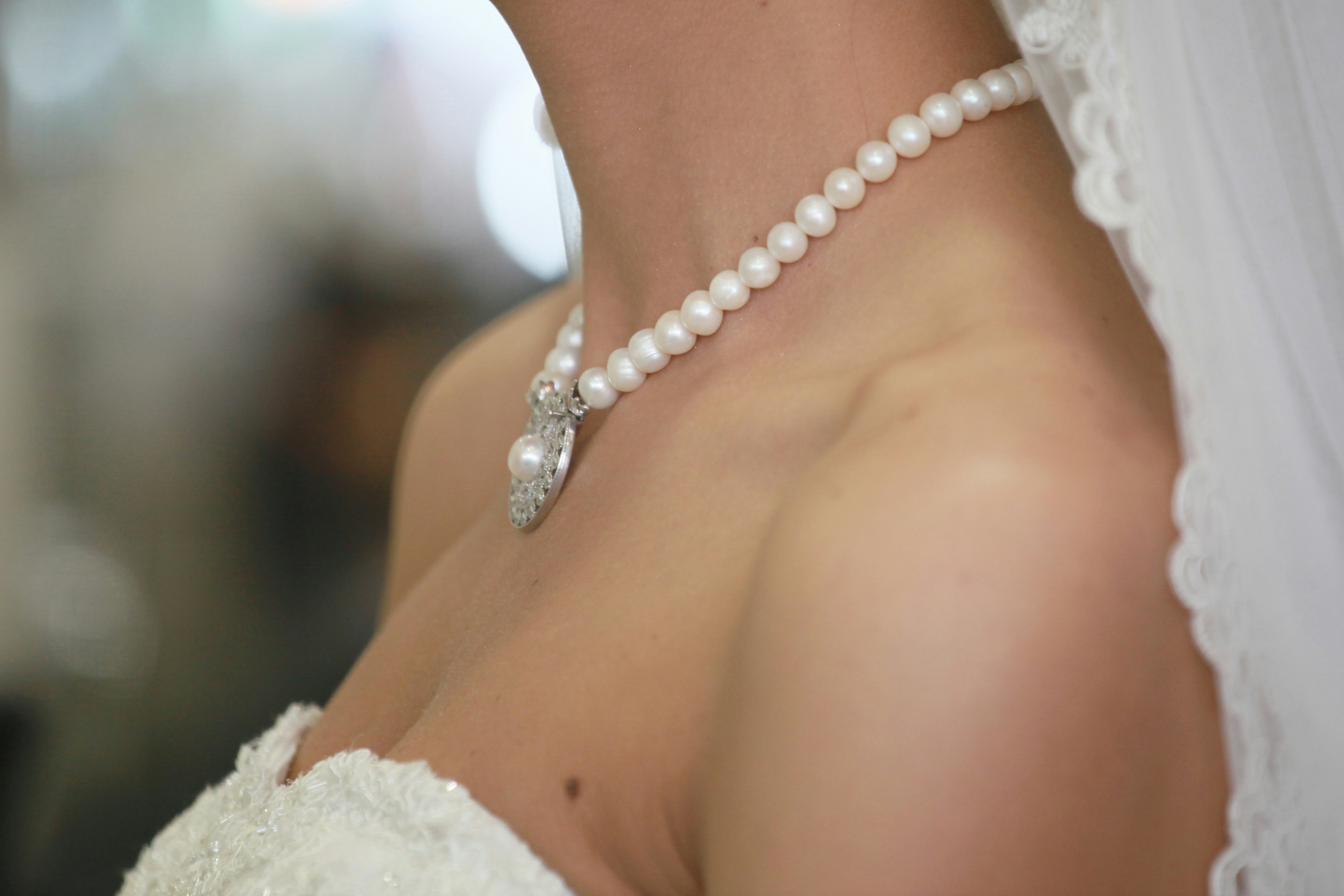 A person wearing a pearl necklace with a silver pendant and lace veil