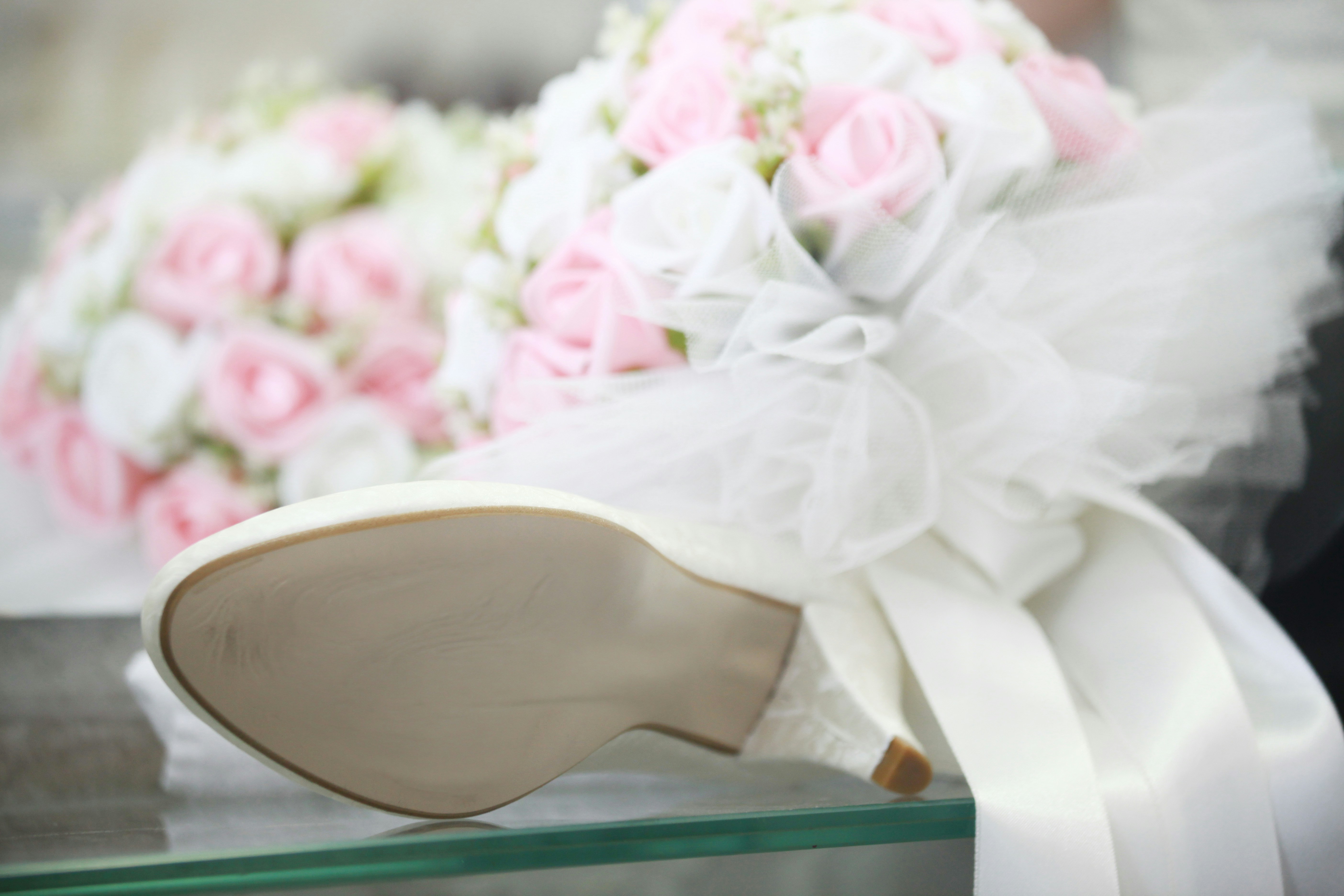 A white bridal shoe beside a bouquet of pink and white roses
