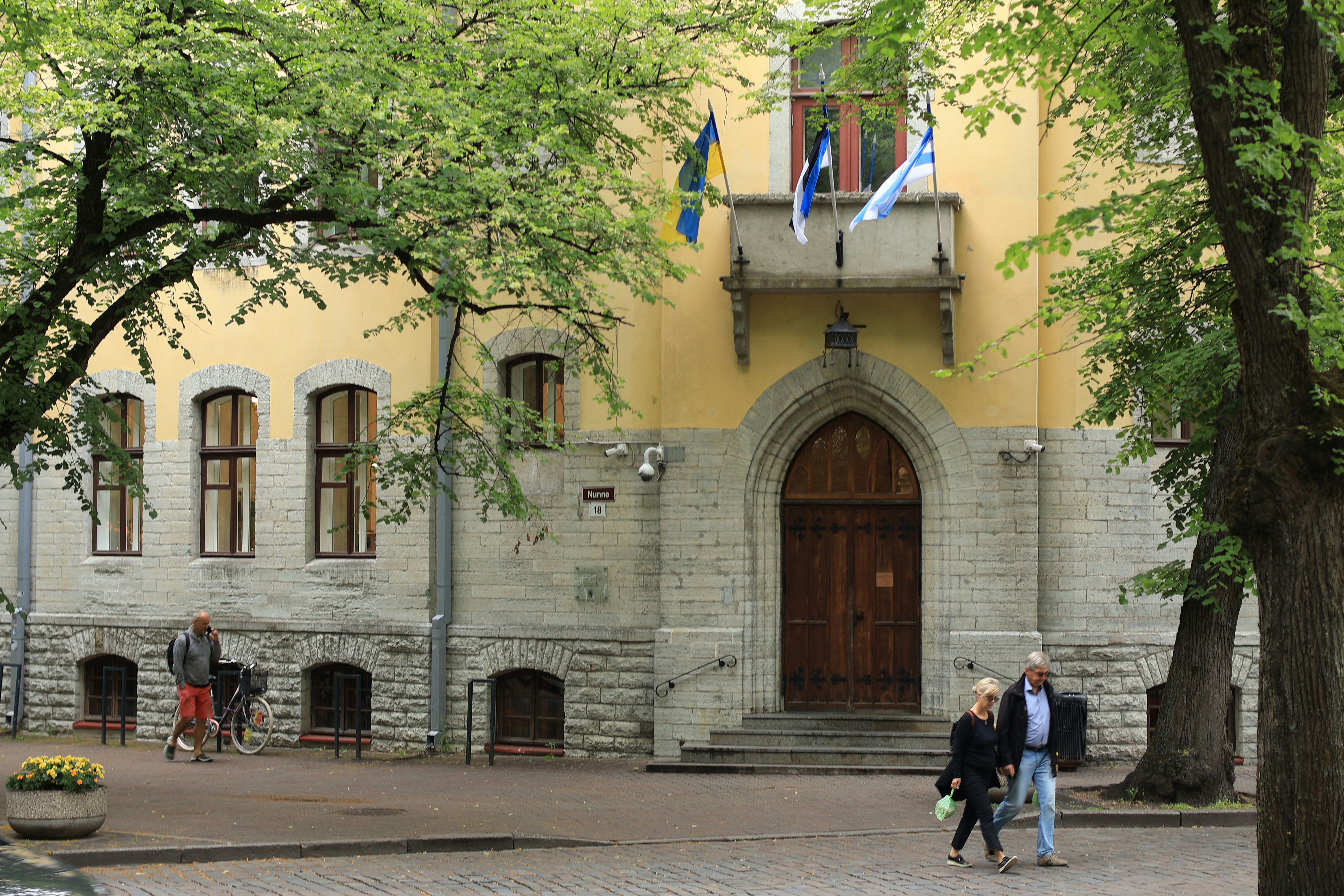 People walking past a yellow stone building with flags on a balcony in Tallinn