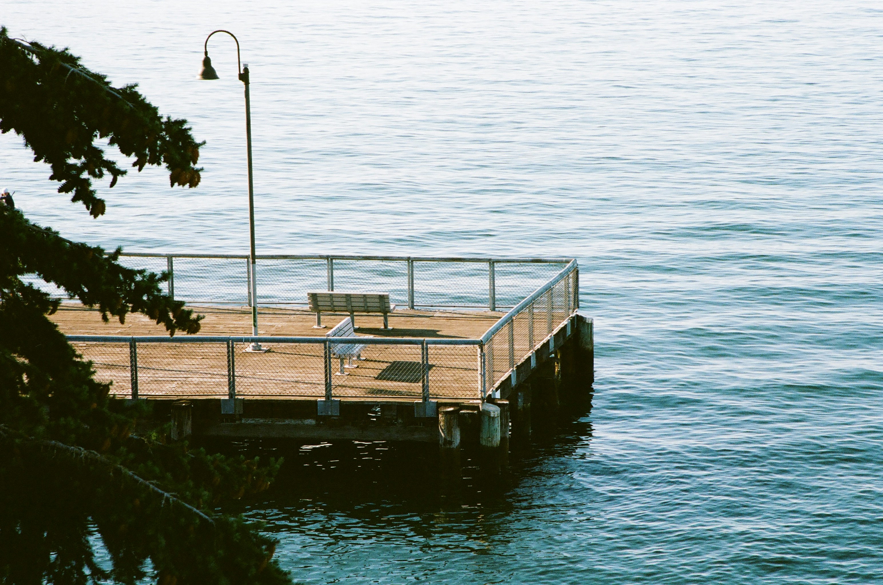 A wooden pier with two benches and a lamp post above calm blue water