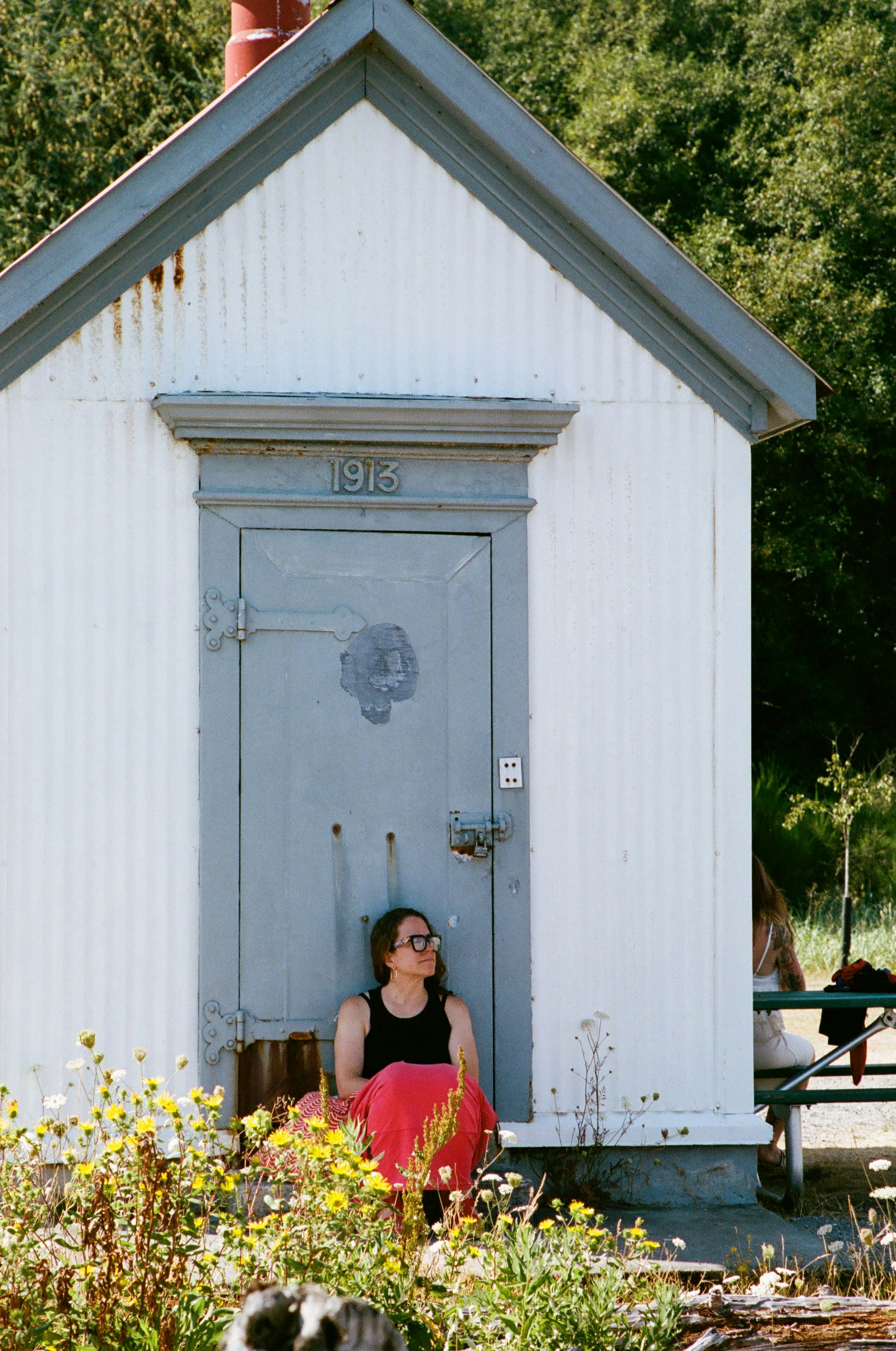 A woman in a black tank top leaning against a white shed door