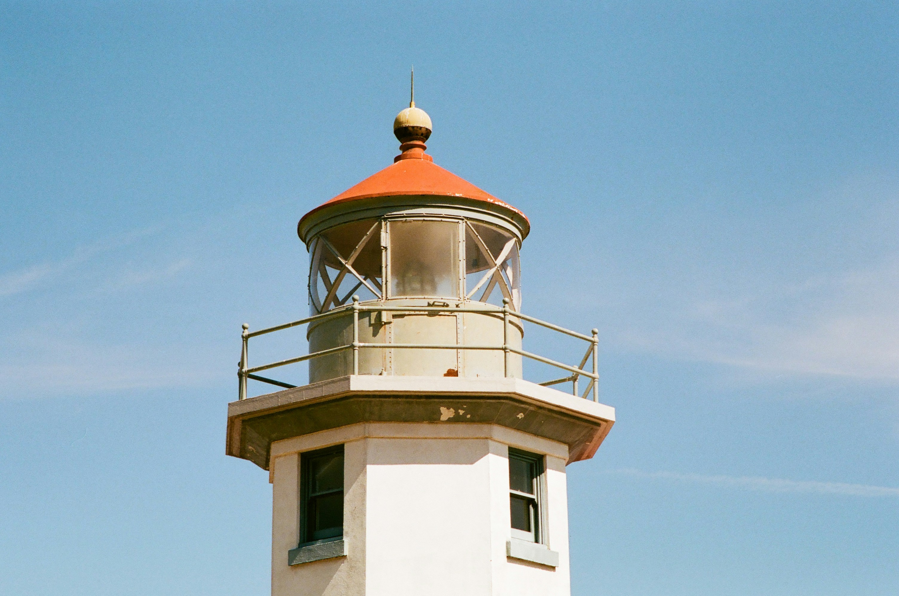 The top of a white lighthouse with a red roof against a blue sky
